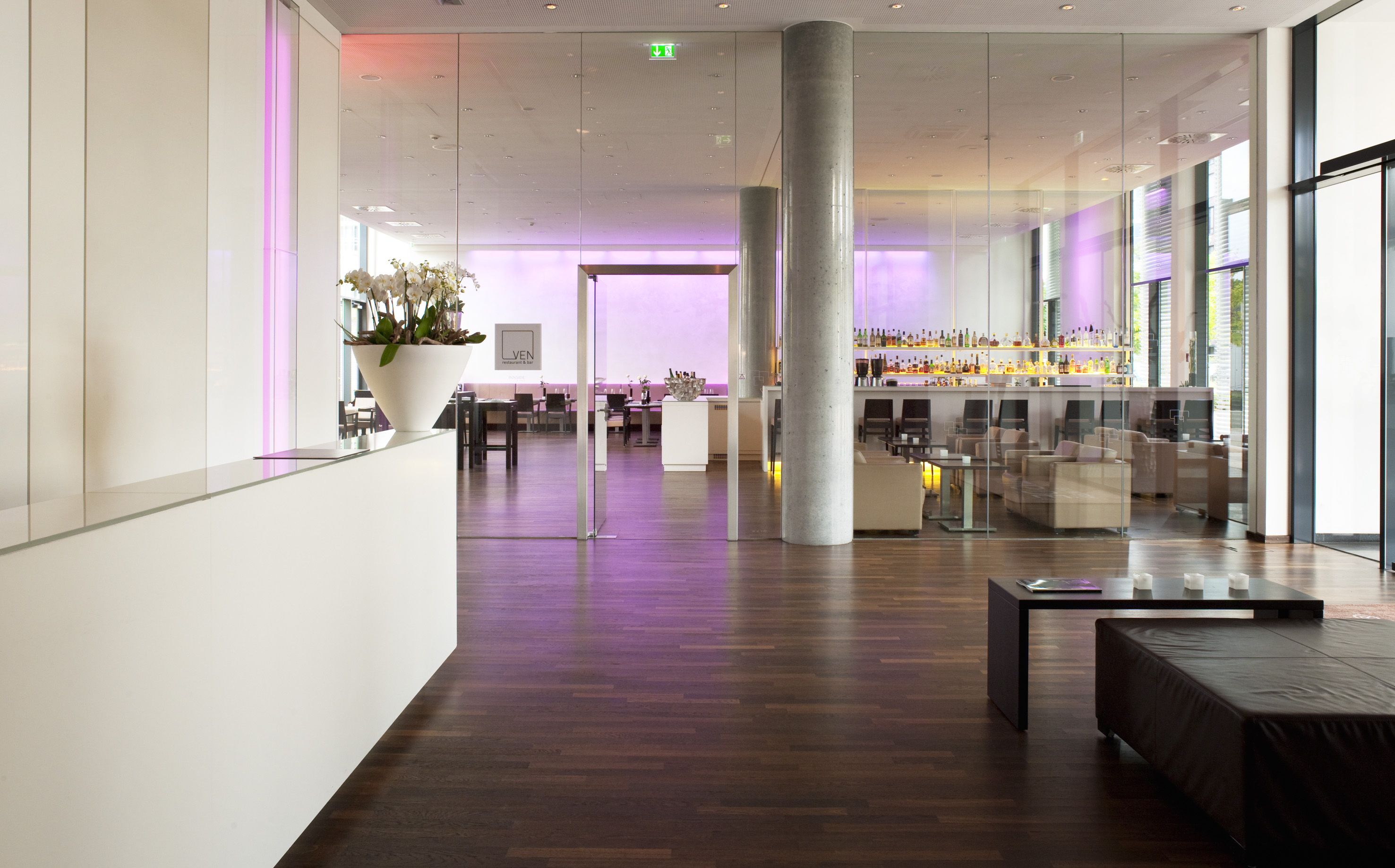 Modern hotel lobby and bar with white reception, glass walls, and lounge seating.