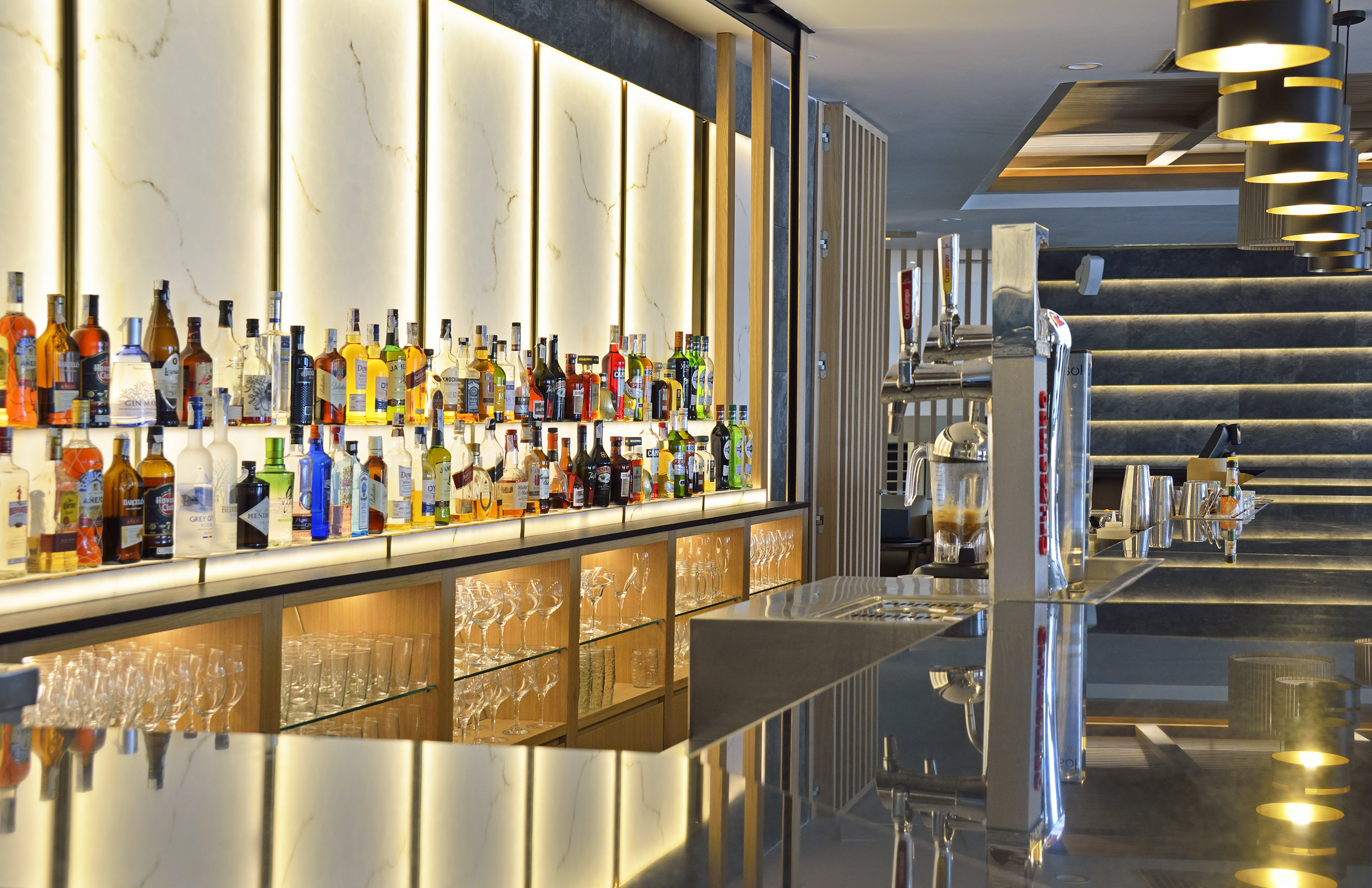 Modern bar with liquor bottles, backlit display, and sleek counter.