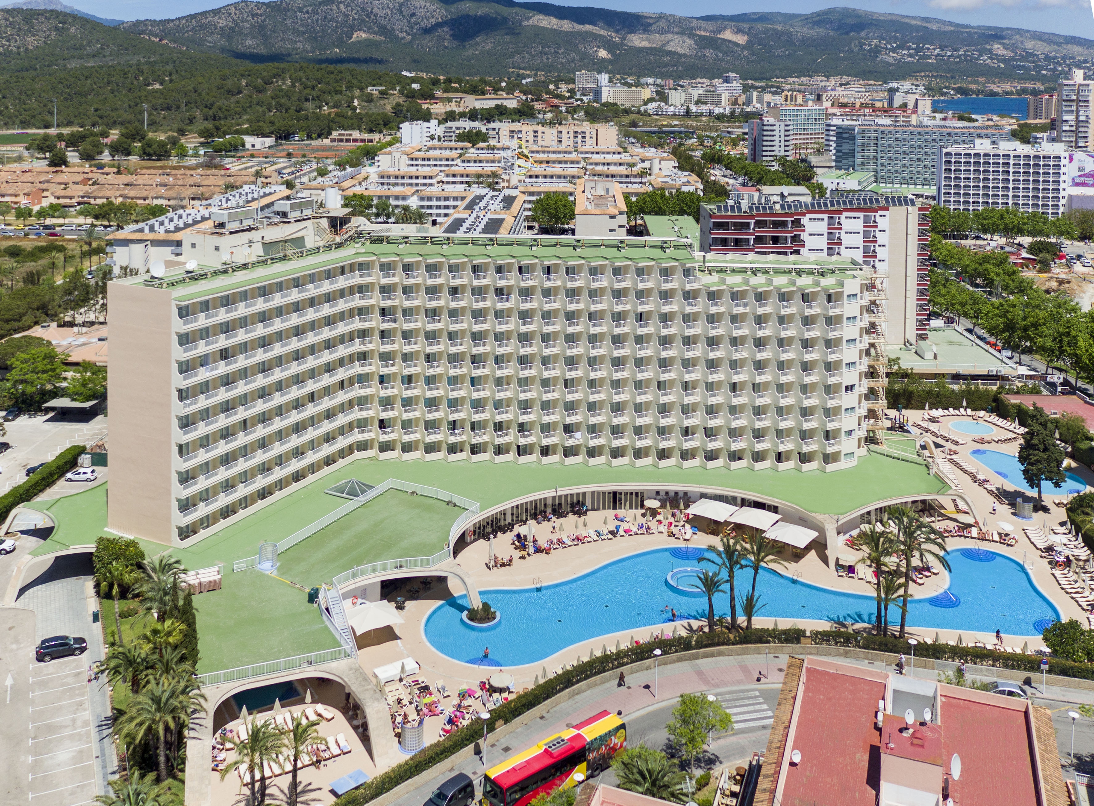 Hotel resort with large swimming pool, palm trees, aerial view, coastal town.