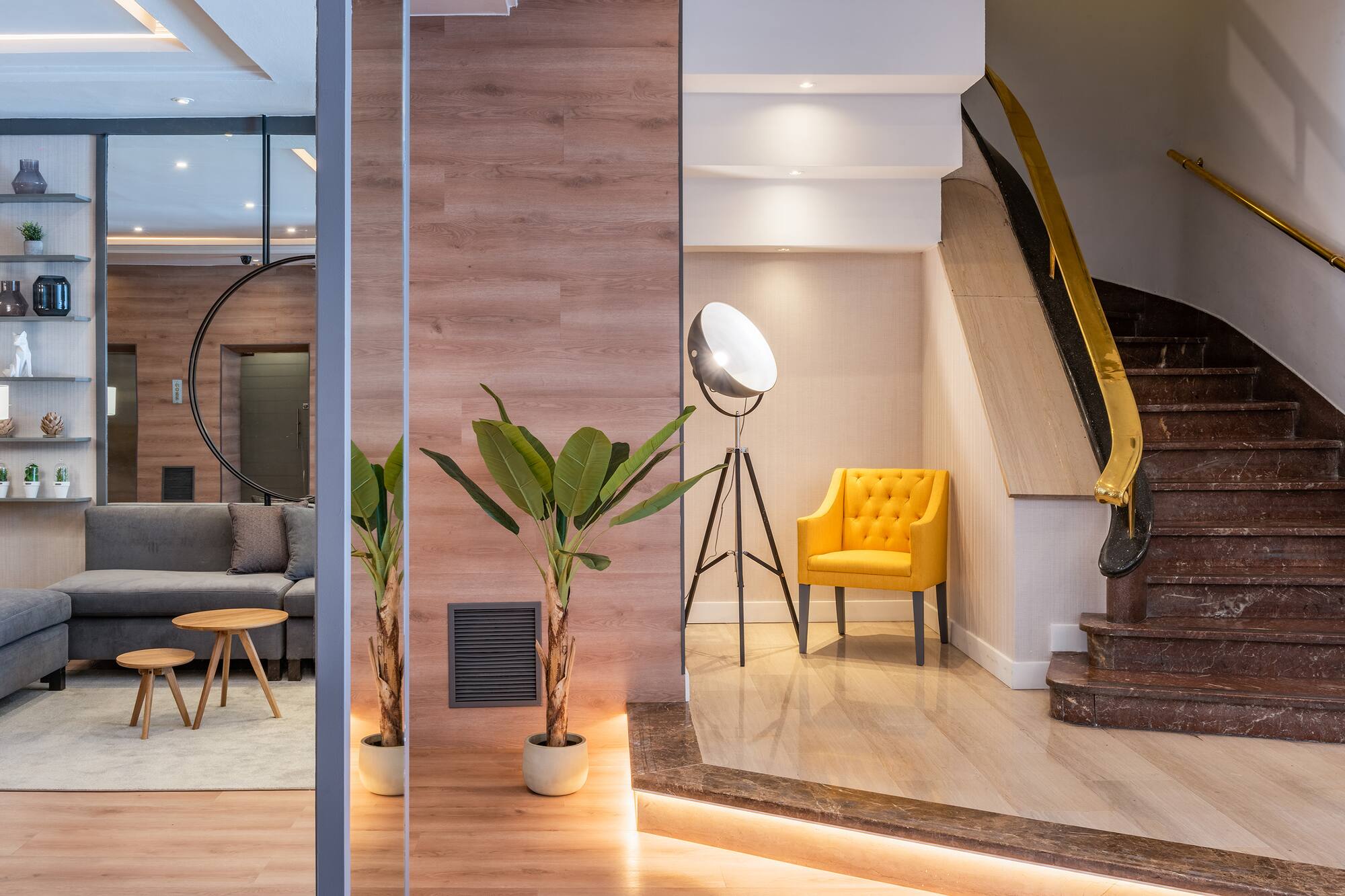 Modern lobby interior with yellow armchair, large plant, and marble staircase.
