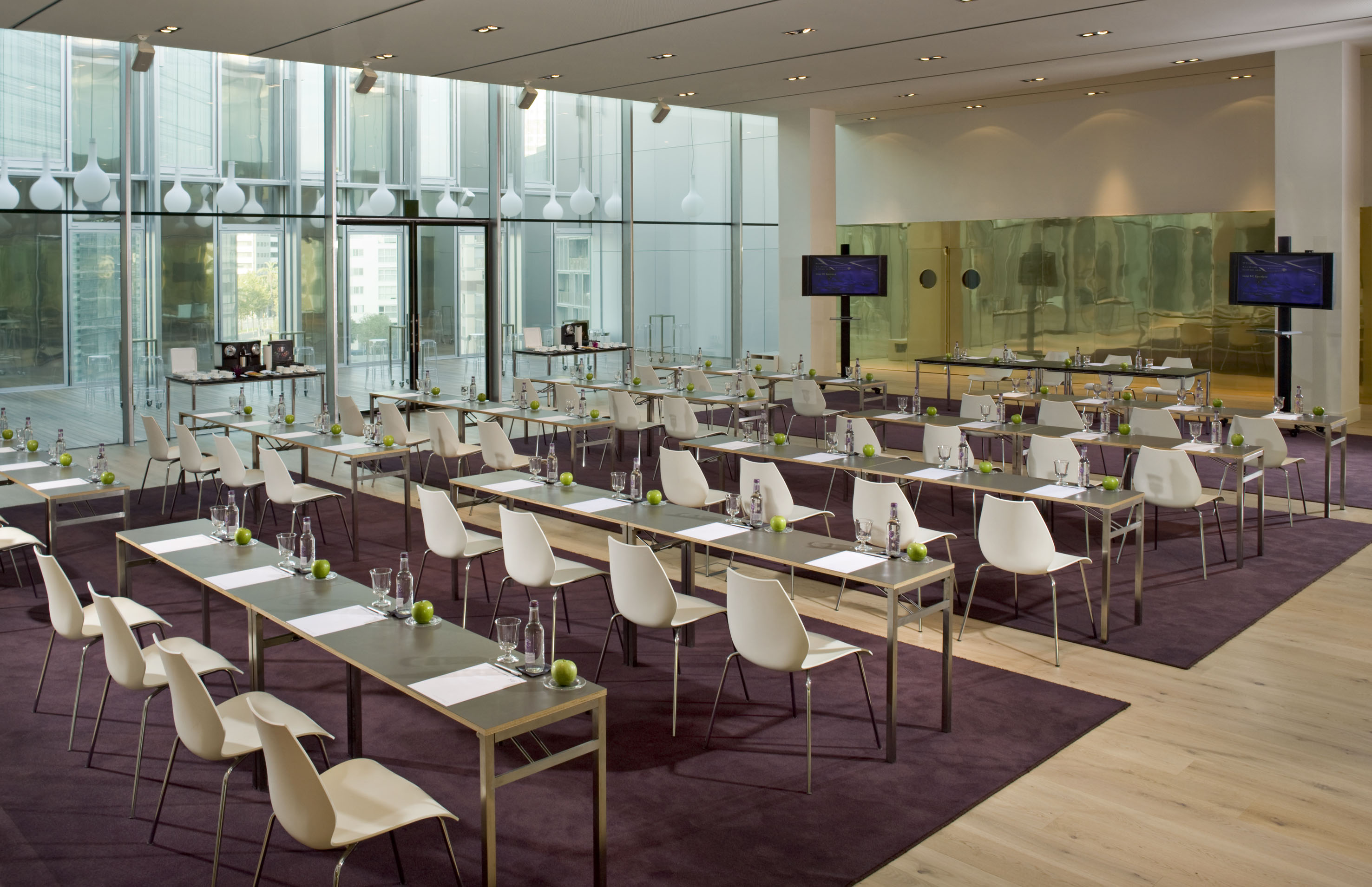 Modern meeting room with rows of tables, chairs, and ample natural light.