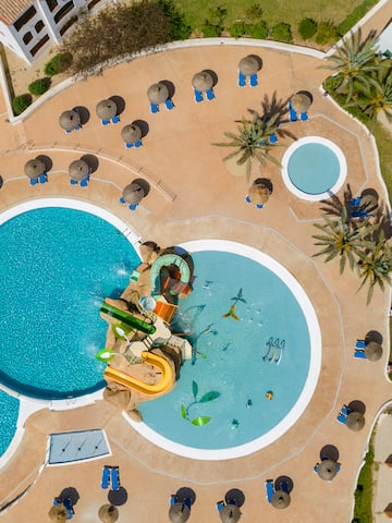 a pool with a slide and a pool with umbrellas and palm trees