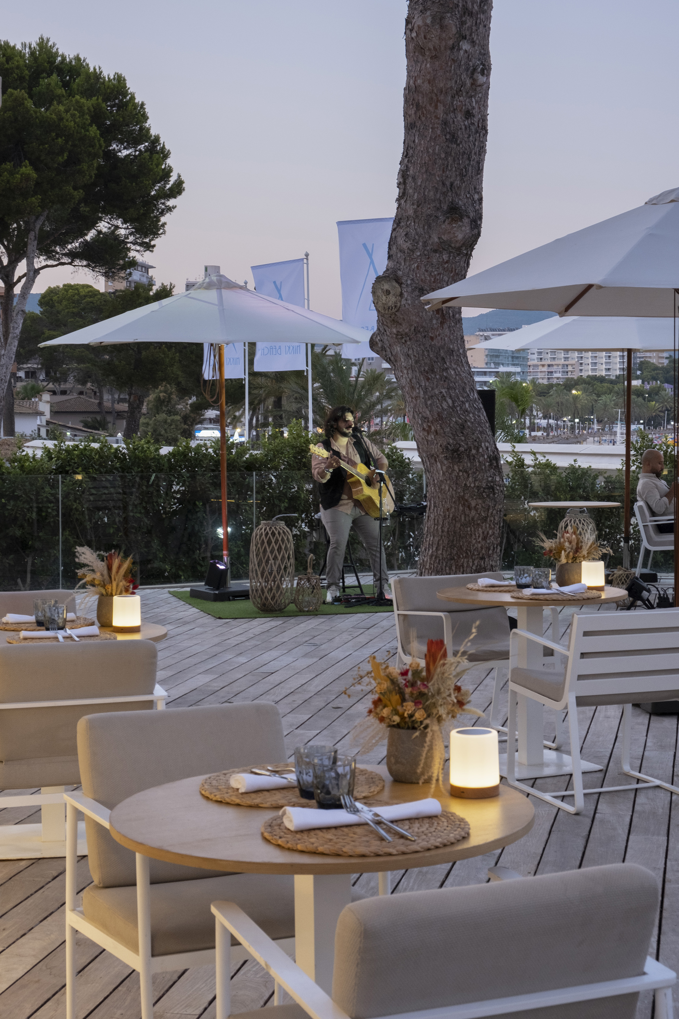 Outdoor dining patio with live guitarist and elegantly set tables at dusk.