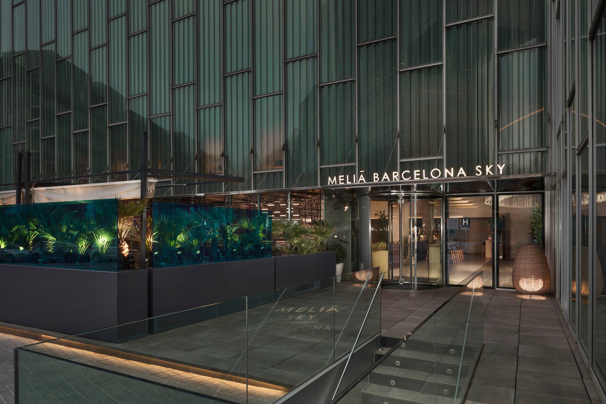 Meliá Barcelona Sky hotel entrance, modern glass building, illuminated greenery.