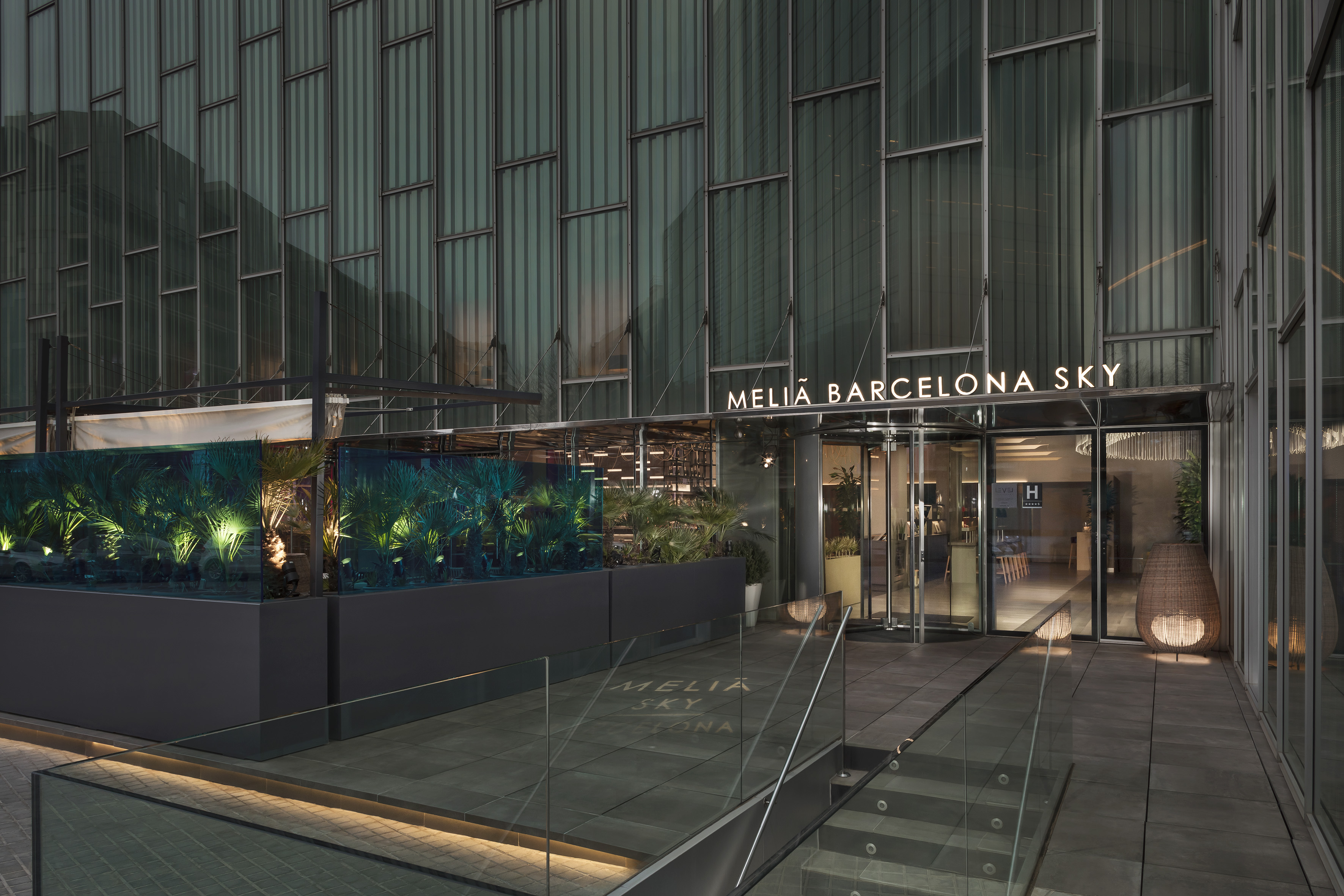 Meliá Barcelona Sky hotel entrance, modern glass building, illuminated greenery.