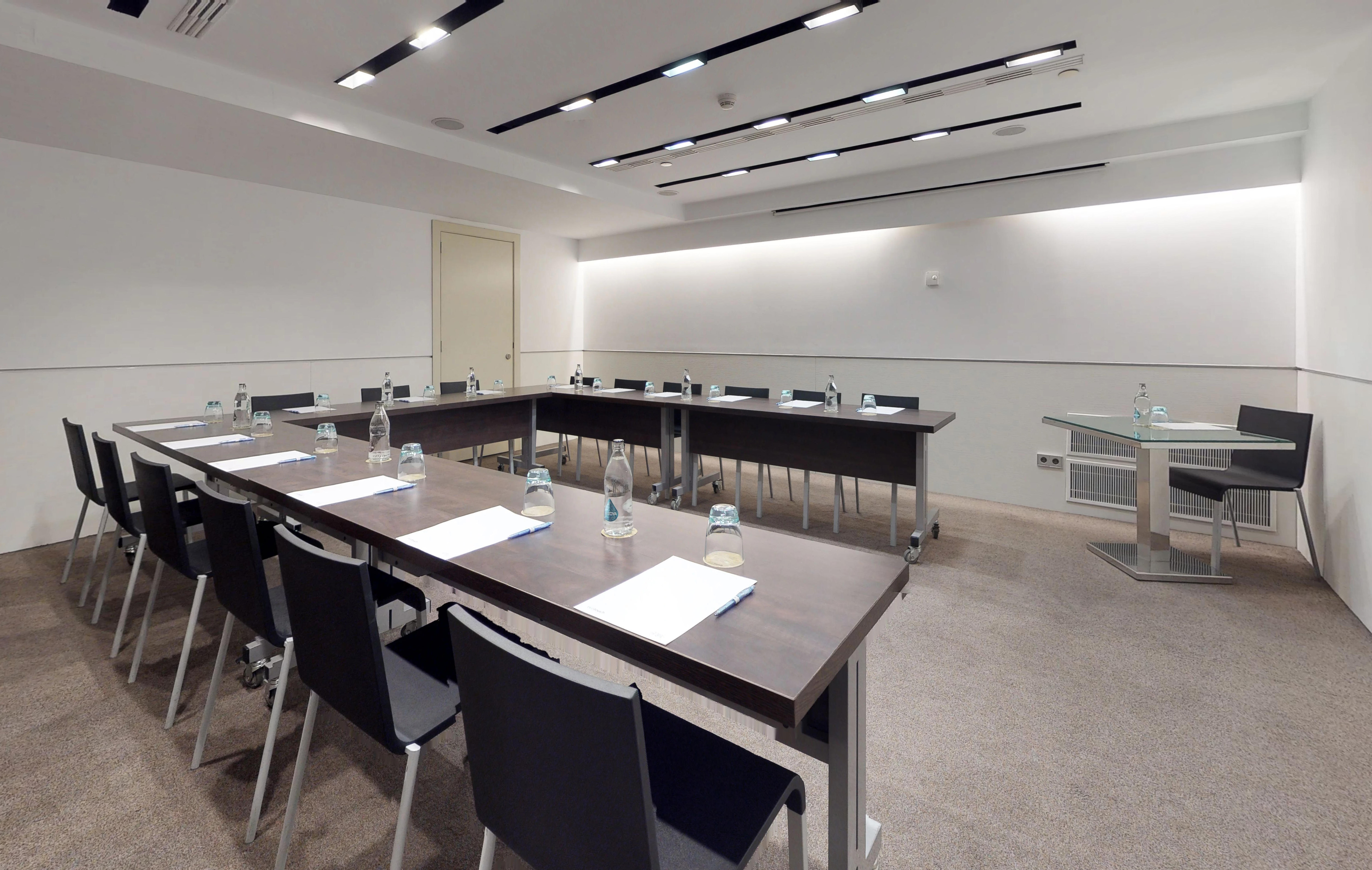 Contemporary conference room with U-shaped table, black chairs, modern lighting.