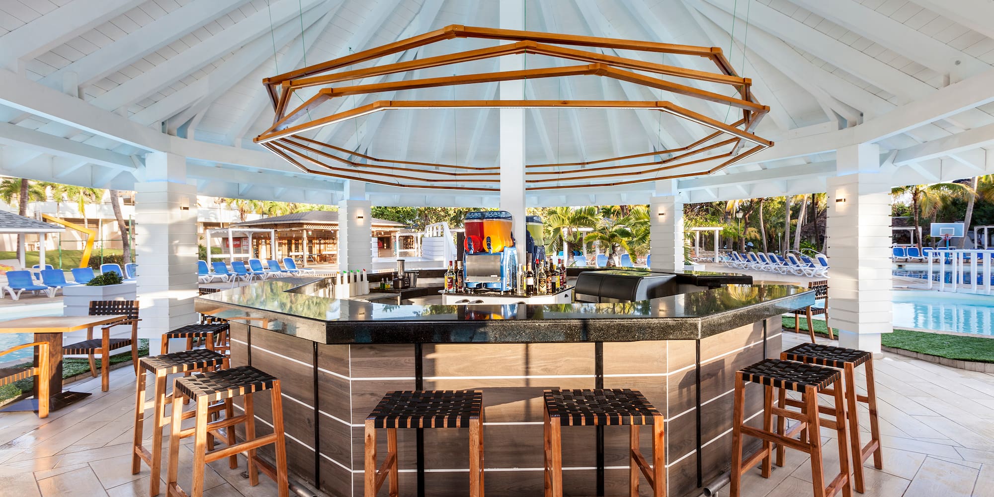 a bar with chairs and a pool in the background