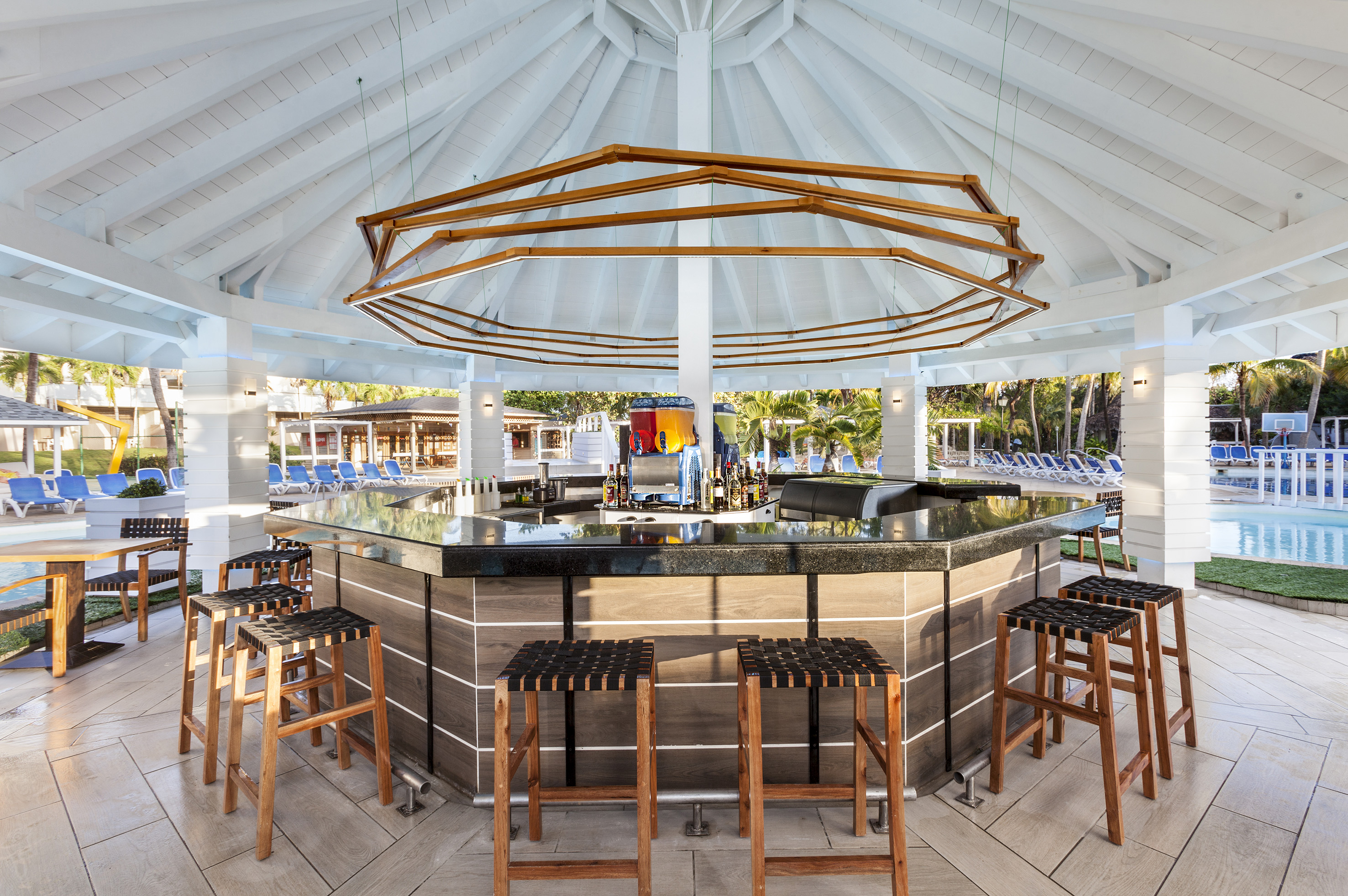 a bar with chairs and a pool in the background