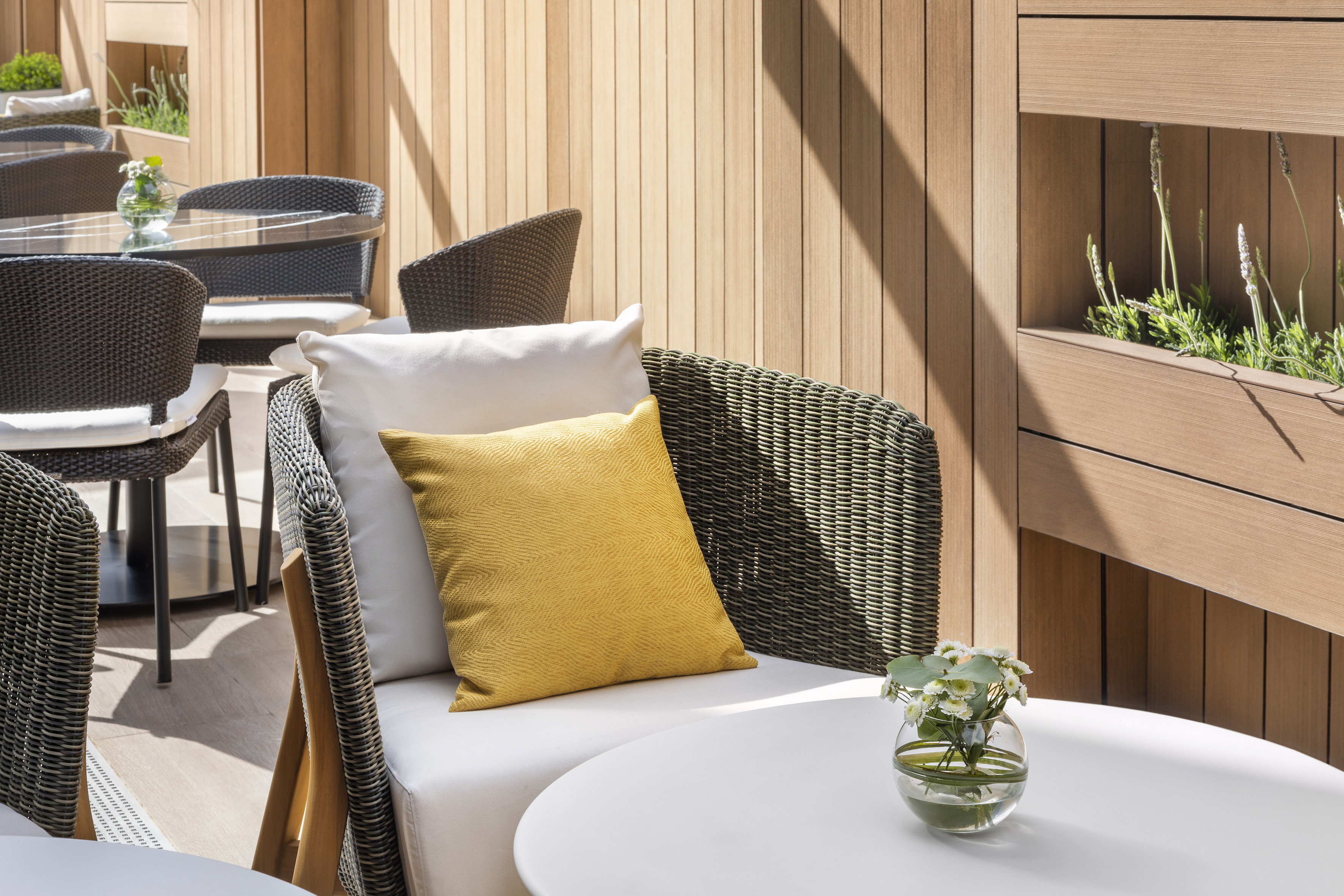 Stylish outdoor patio with wicker seating, yellow cushion, wood wall, and flowers.