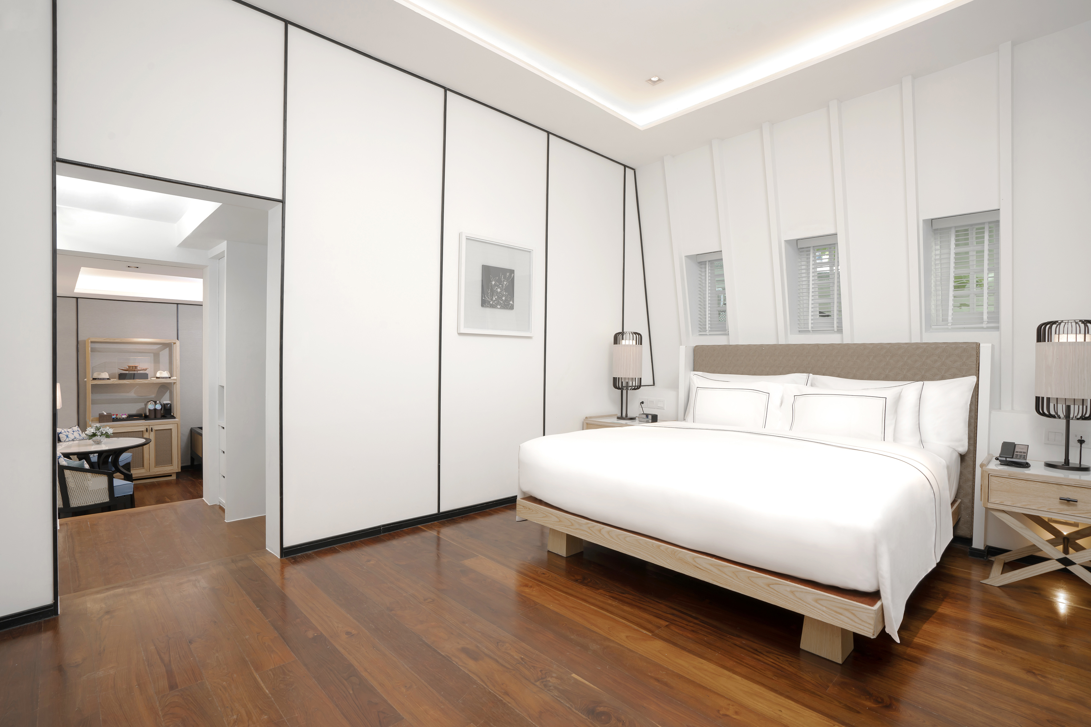 Bright modern hotel bedroom with white bed, wood floor, and minimalist decor.