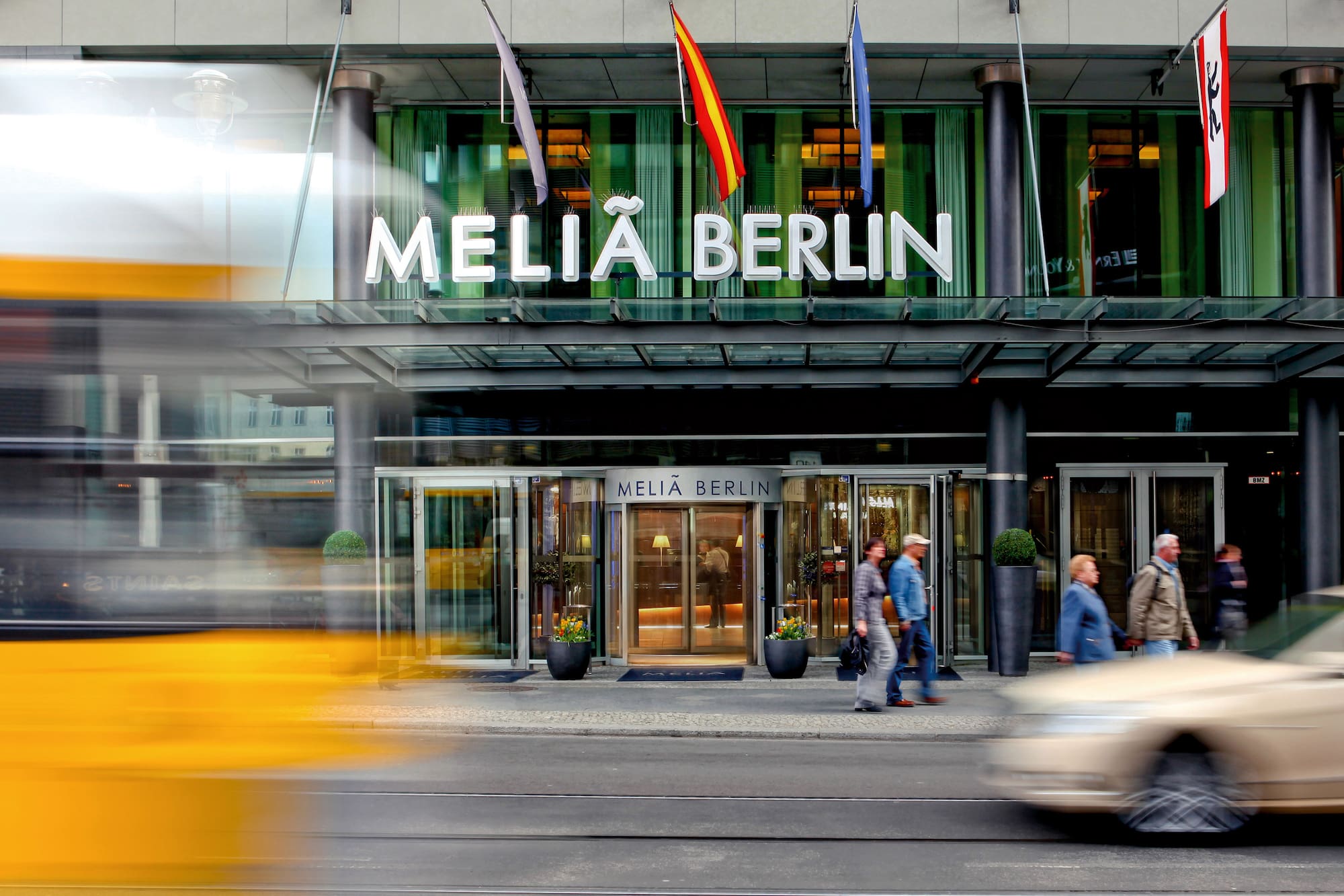 Melia Berlin hotel entrance, flags, pedestrians, blurred street traffic.