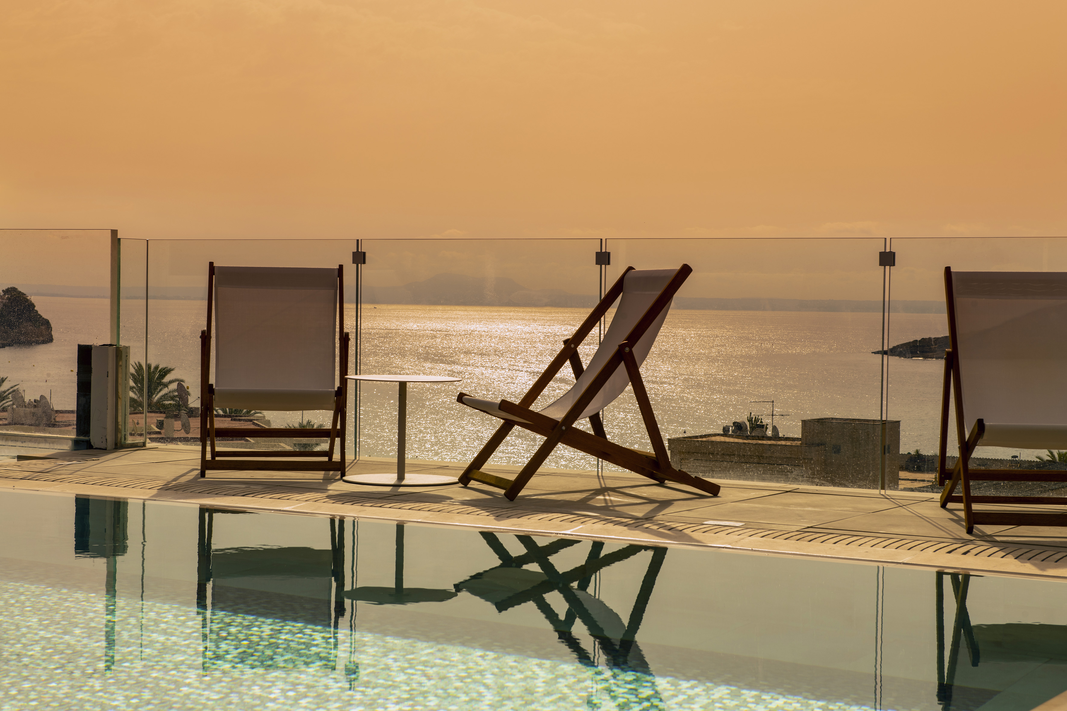 Infinity pool, lounge chairs, and glittering ocean view at sunset.