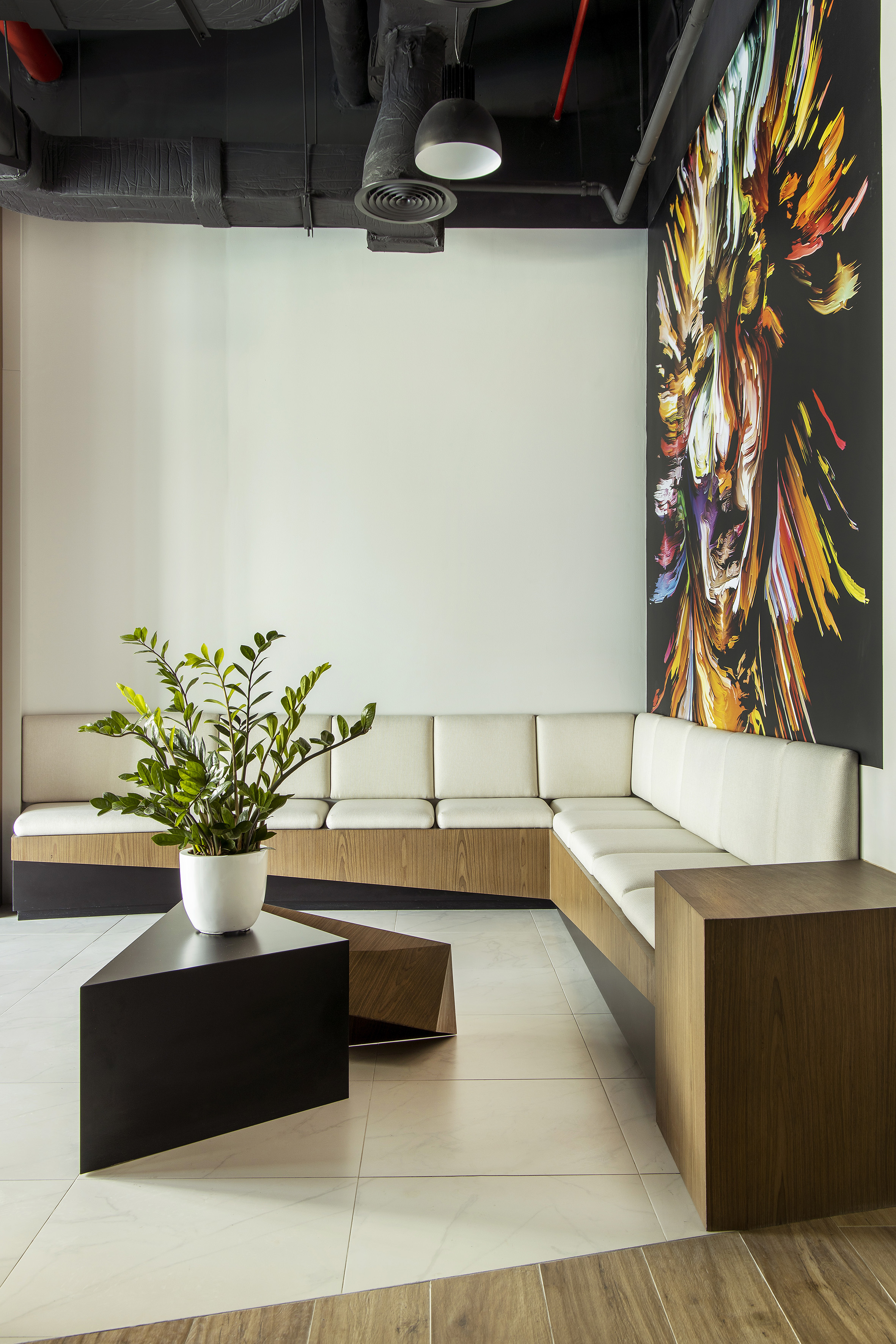Modern office lobby with L-shaped wood sofa, abstract art, coffee tables.