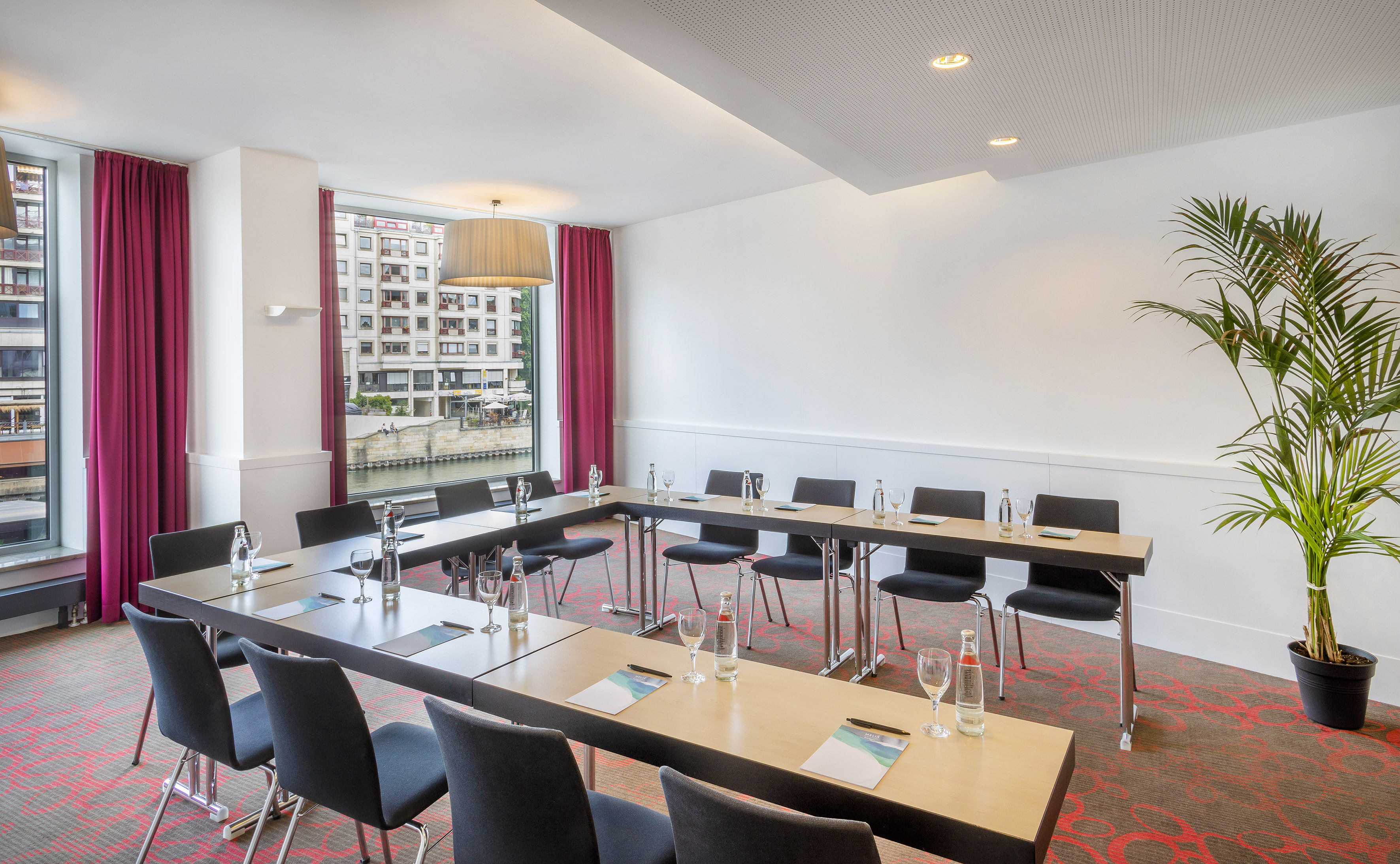 Modern conference room with U-shaped table, black chairs, and waterfront view.
