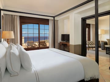 a bed with white sheets and a mirror in a room with a view of the ocean