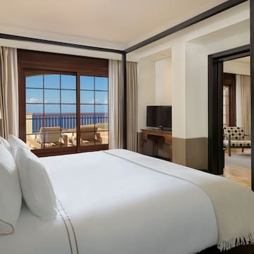 a bed with white sheets and a mirror in a room with a view of the ocean
