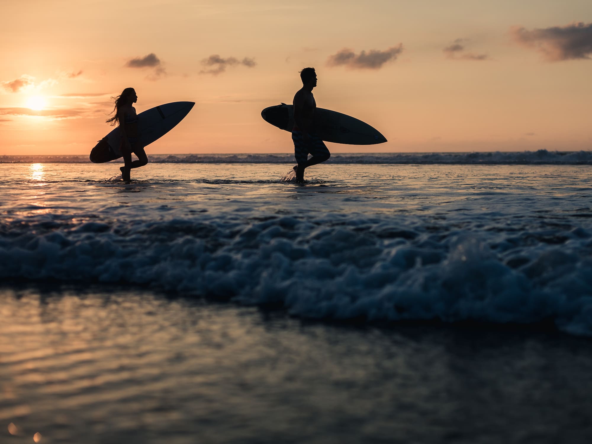 a man and woman carrying surfboards in water