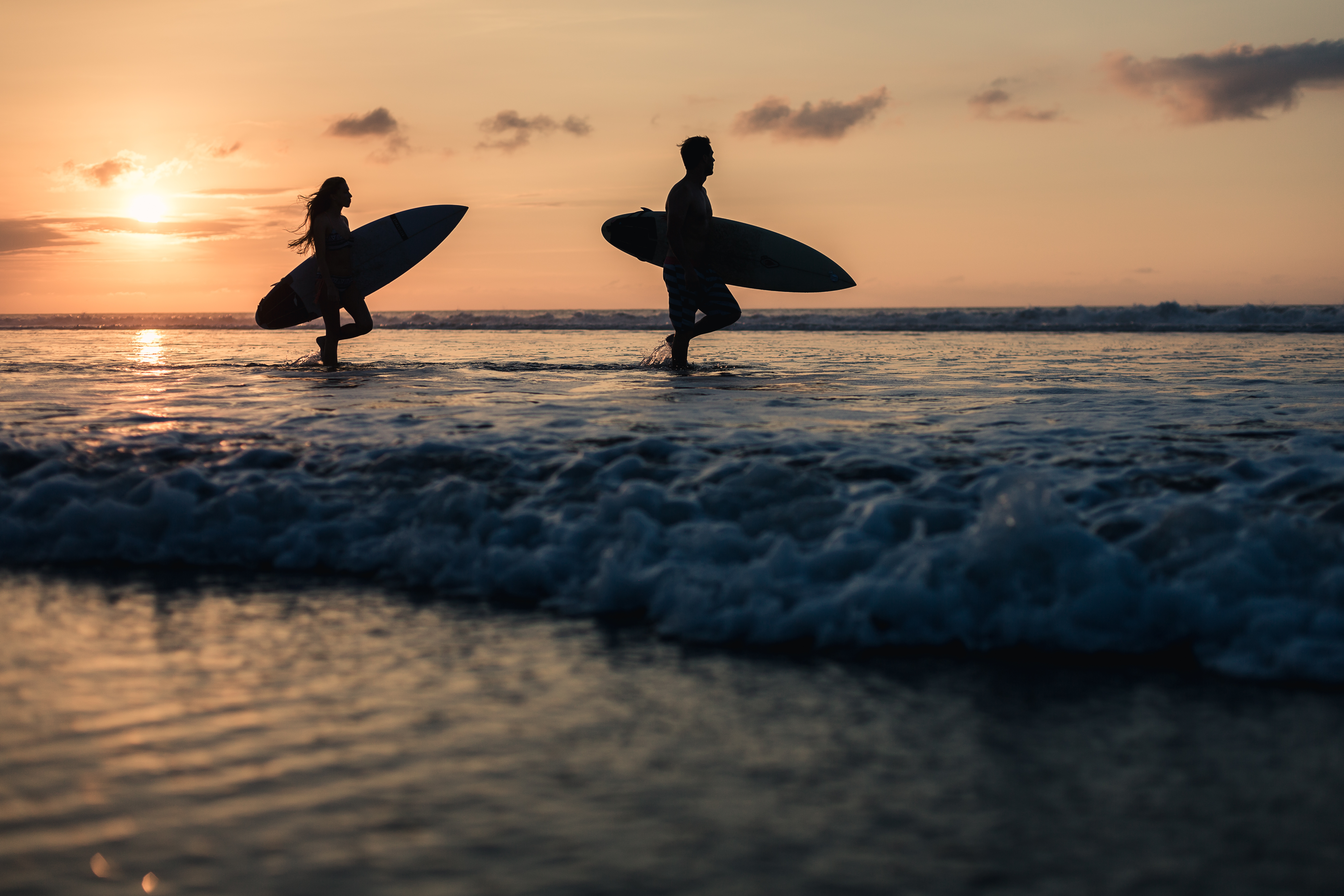 a man and woman carrying surfboards in water