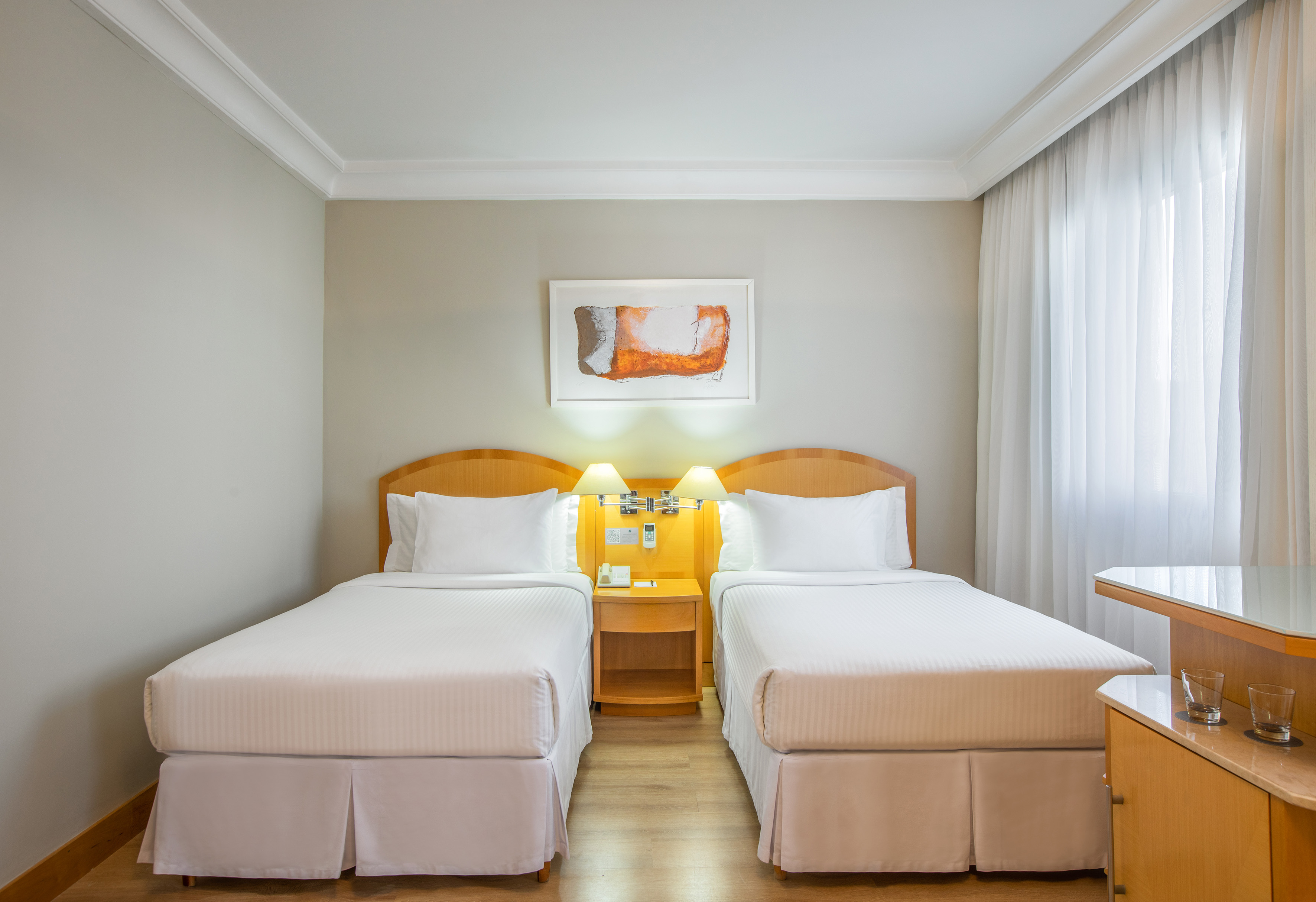 Hotel room with two twin beds, white linens, nightstand, and modern art.