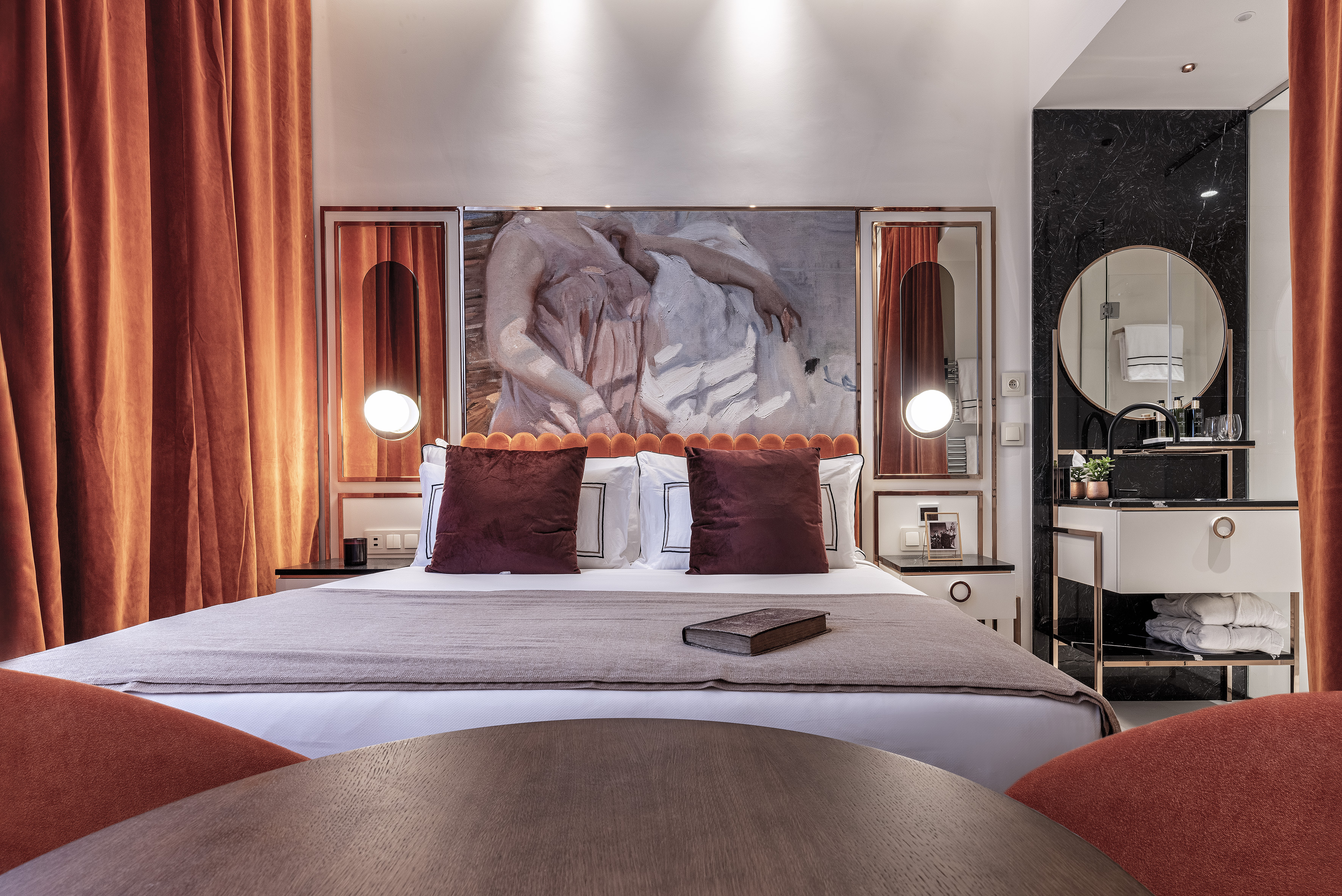 Stylish hotel room with orange velvet, large artwork, and modern vanity.