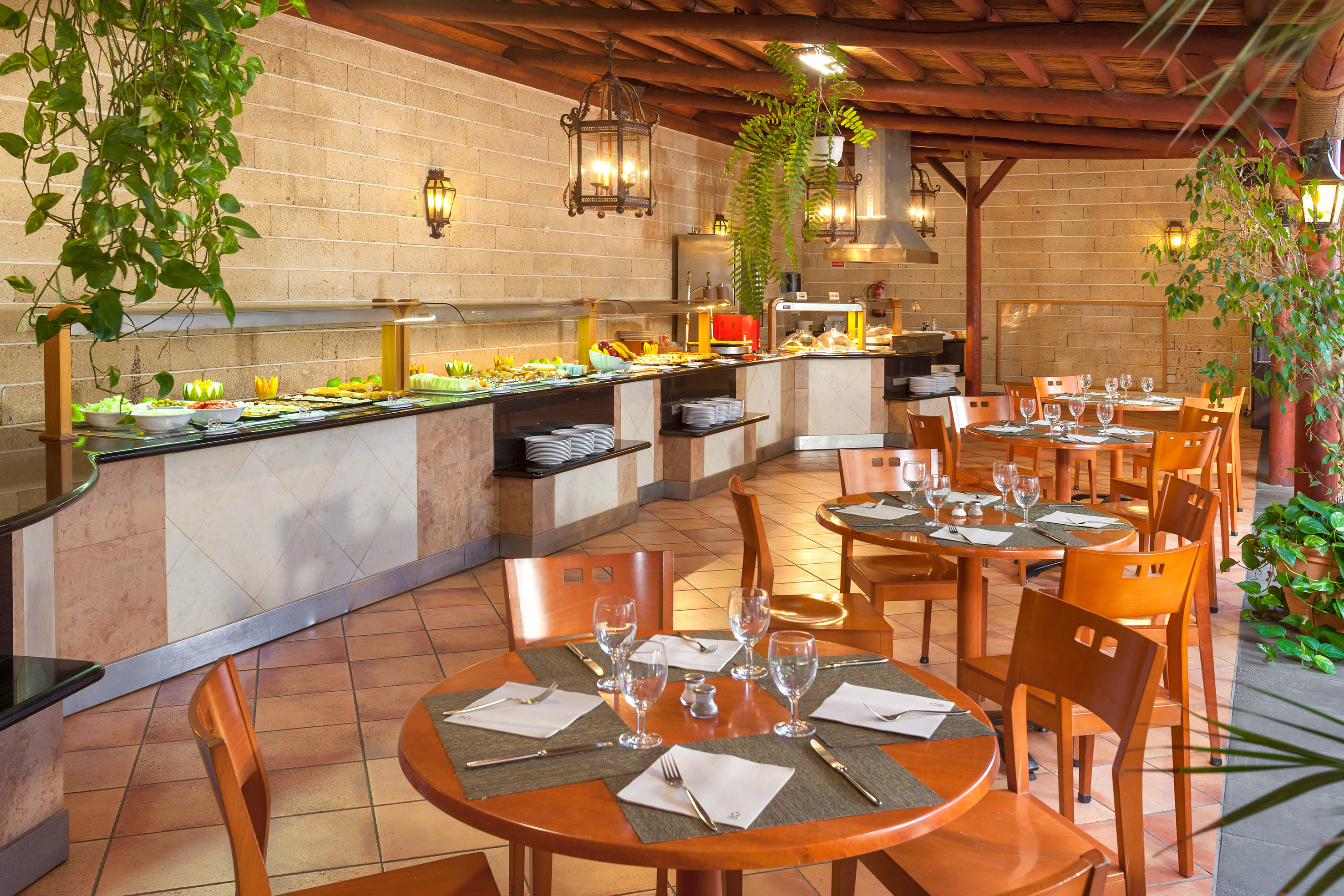 Inviting buffet restaurant with varied dishes, round wooden tables, and hanging plants.
