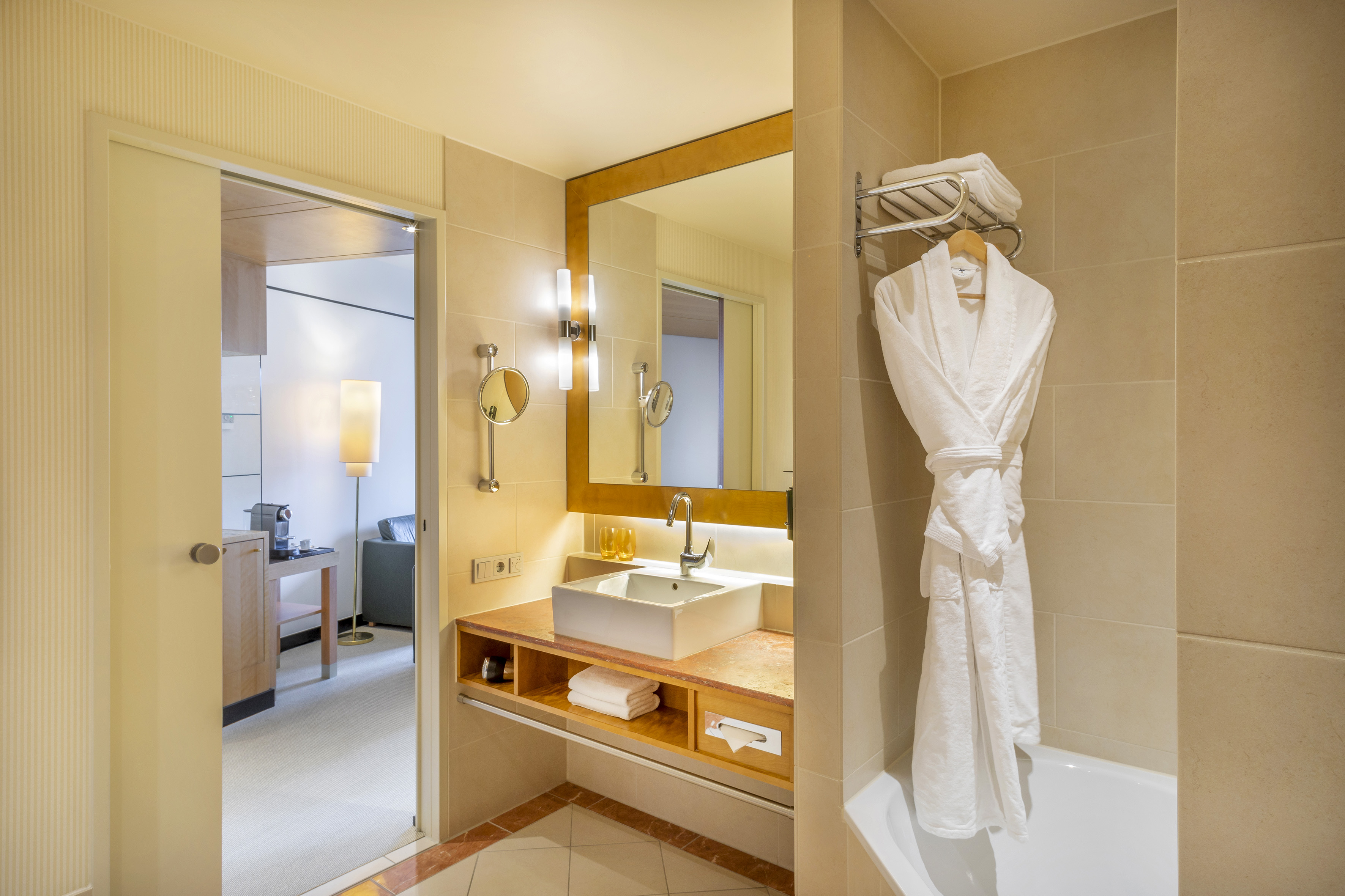 Hotel bathroom vanity with sink, large mirror, bathrobe, and doorway to suite.