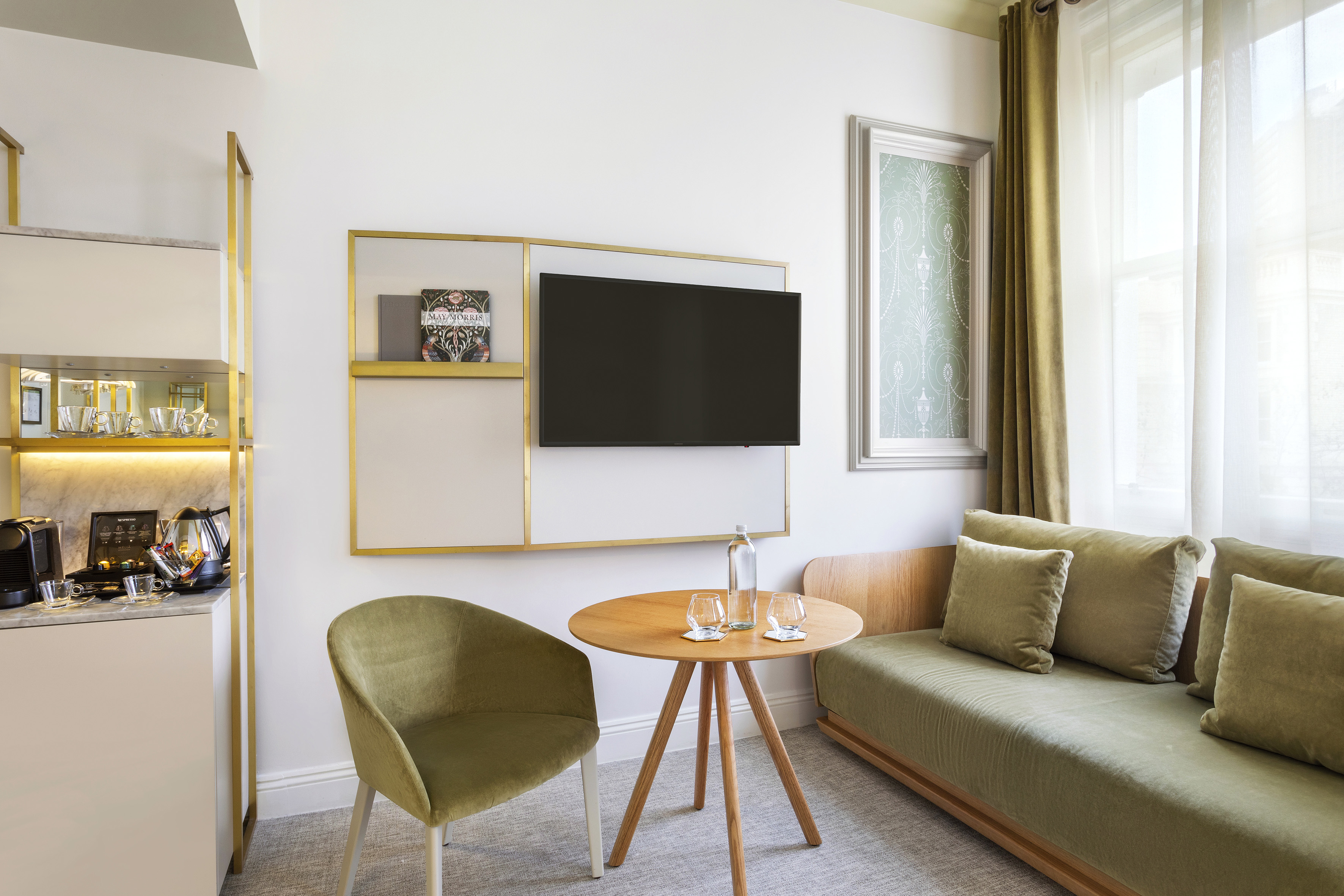 Modern hotel suite living area with olive green sofa, chair, TV, coffee station.