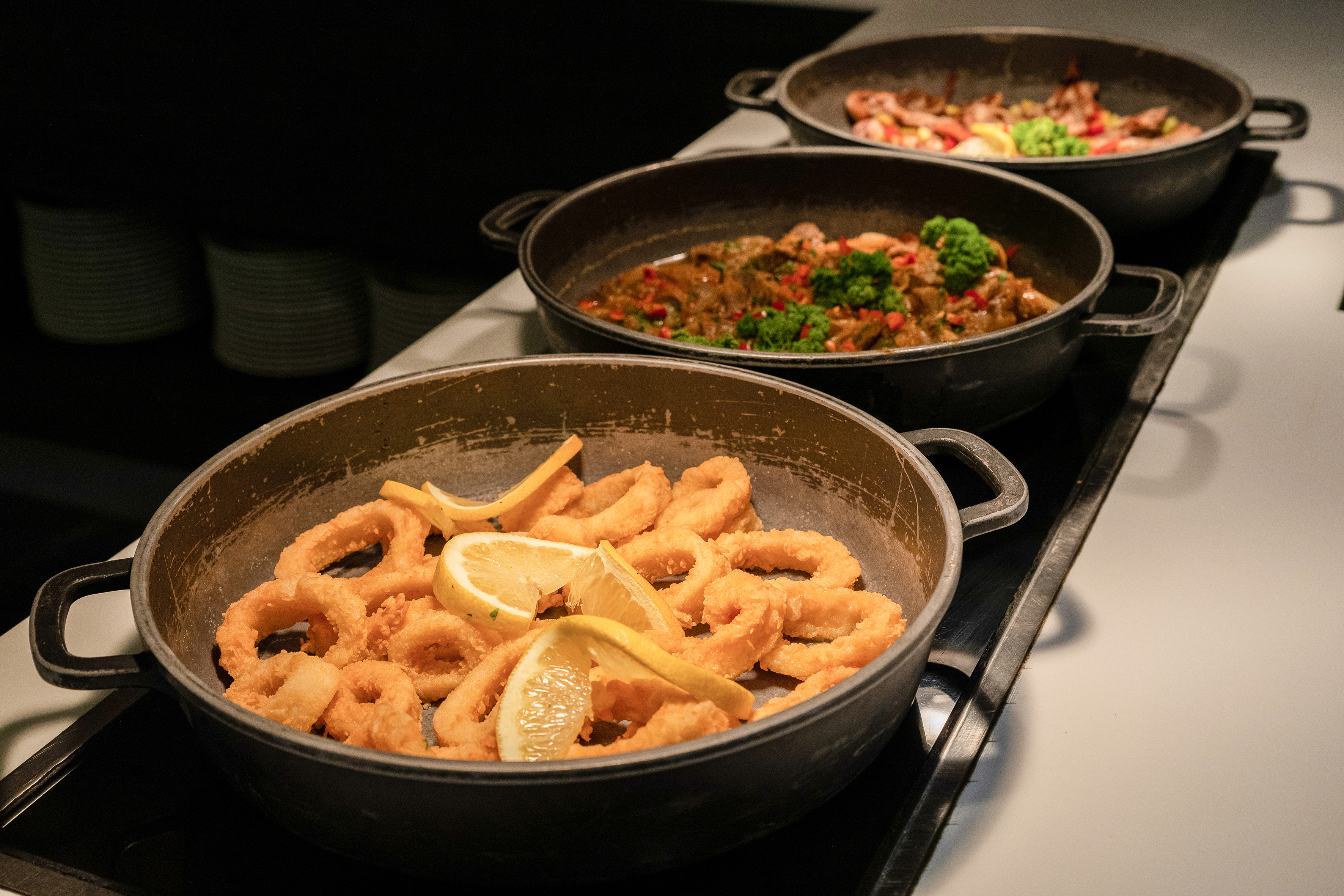 Golden fried calamari, meat stew, and vegetable curry on a hot food buffet.