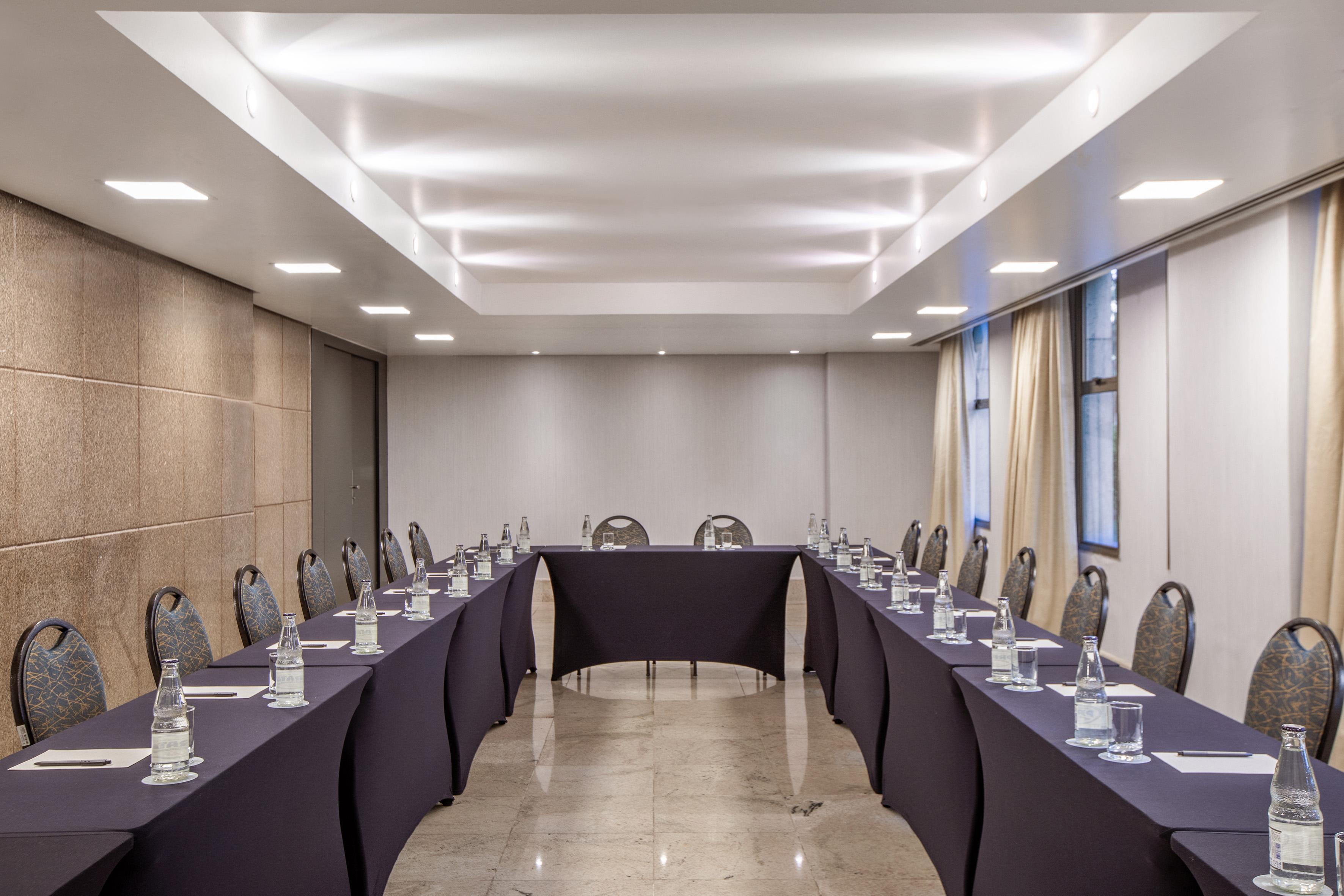 U-shape conference room with tables, chairs, bottled water, and modern lighting. - Encontro IV - -Hotel Madrid Airport Suites Affiliated by Meliá:, Brasilia