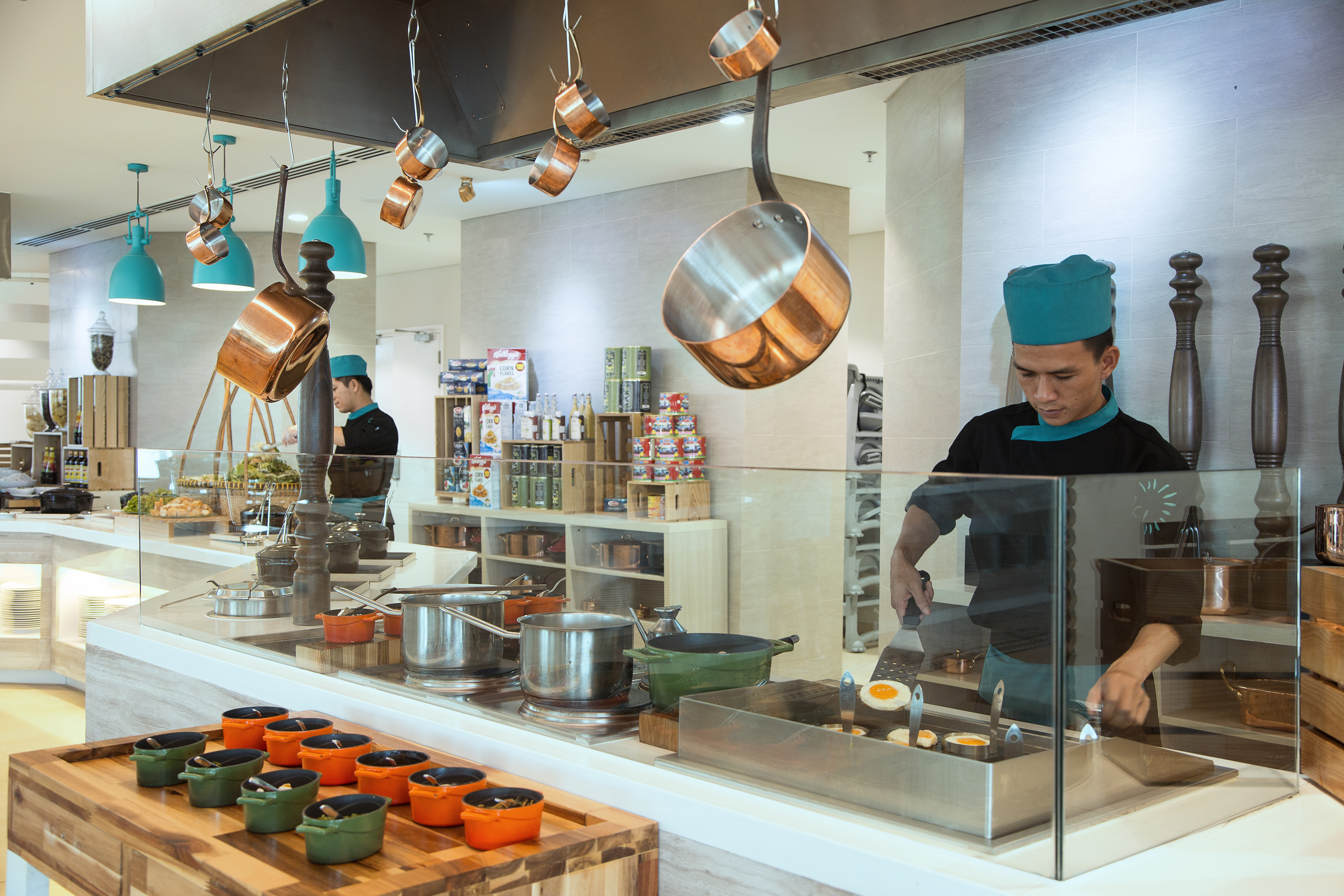 Chef cooking eggs at a hotel breakfast buffet live station with hanging copper pots.