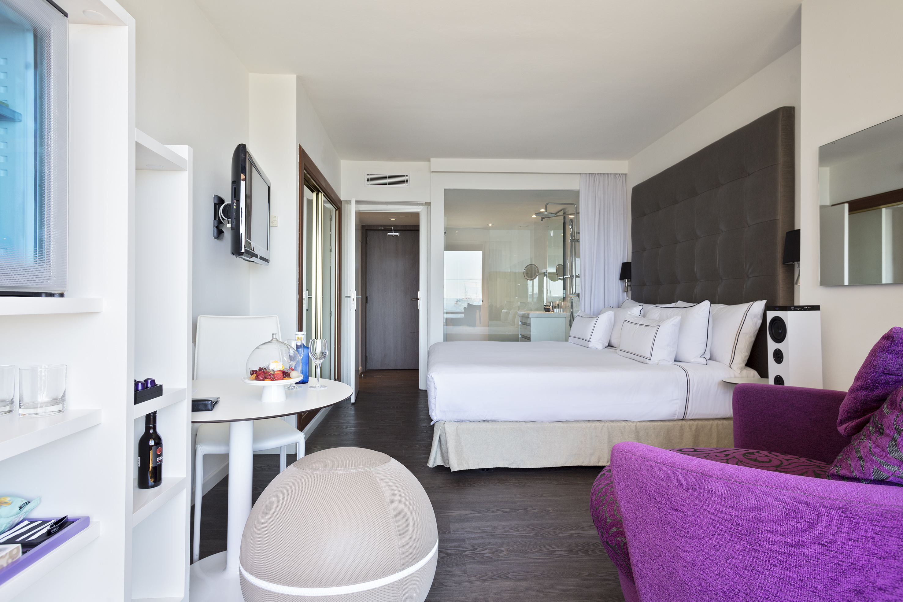 Modern hotel suite with king bed, purple armchair, dining area, and TV.