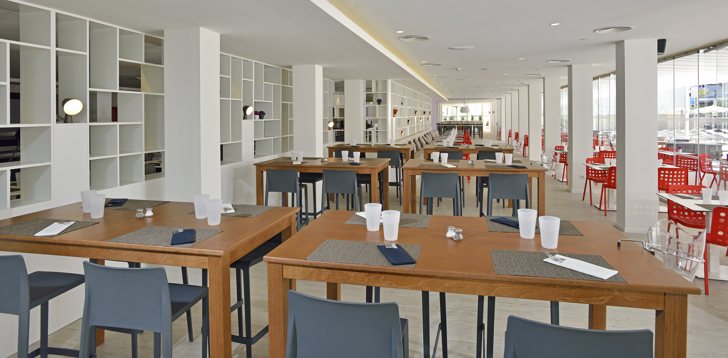 Spacious modern dining room with wooden tables, grey chairs, white shelving.