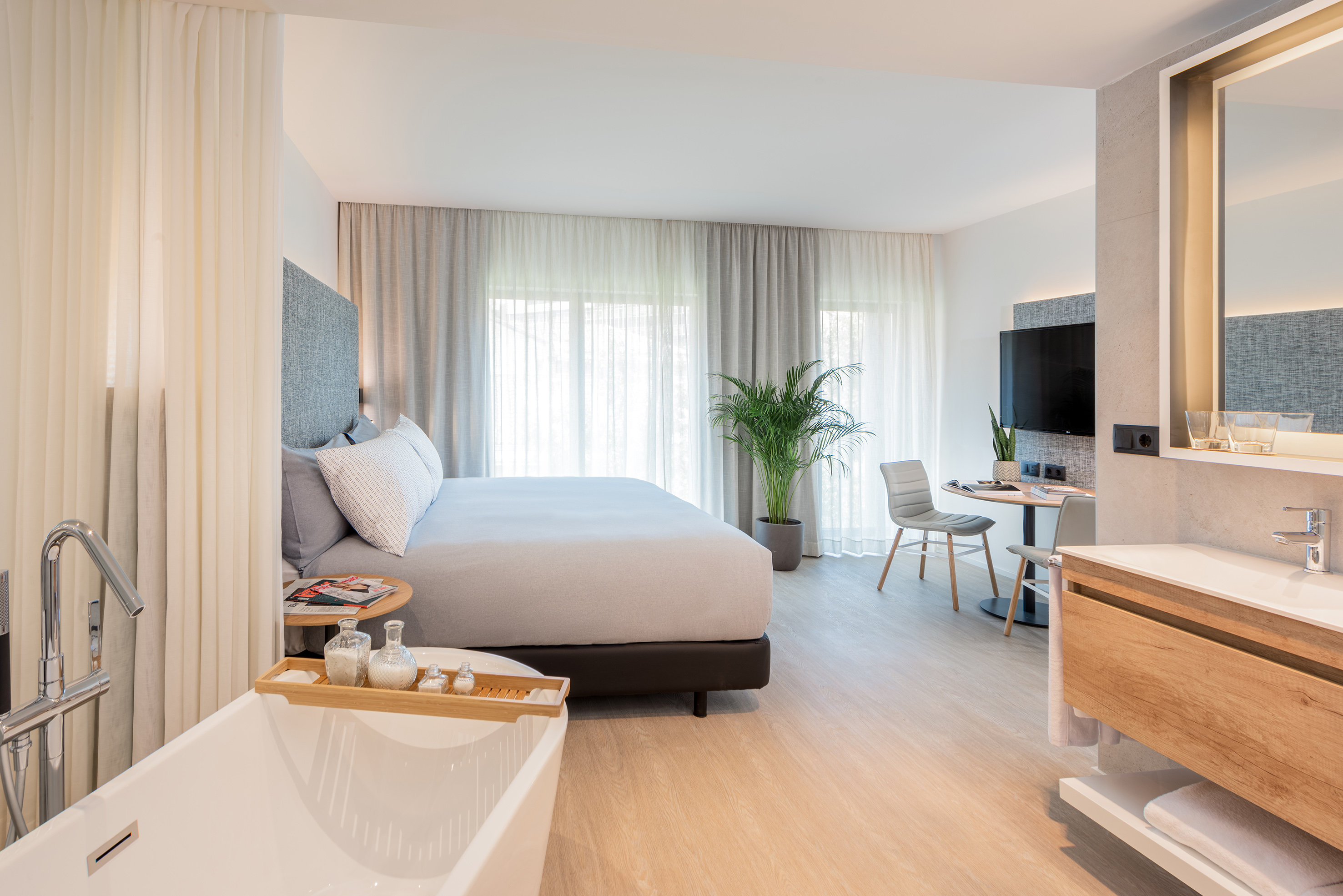 Modern hotel suite with king bed, open bathtub, vanity, and sitting area.