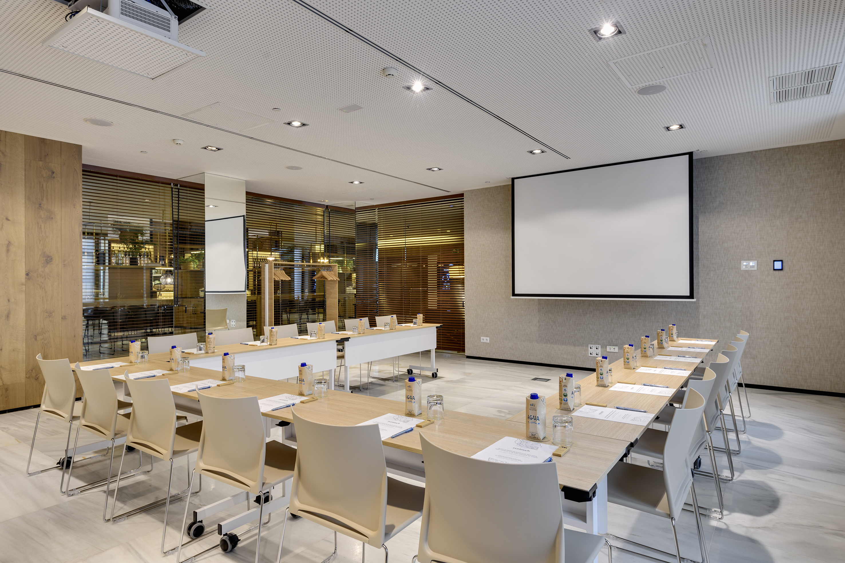Modern conference room with projector screen, U-shaped tables, and chairs.