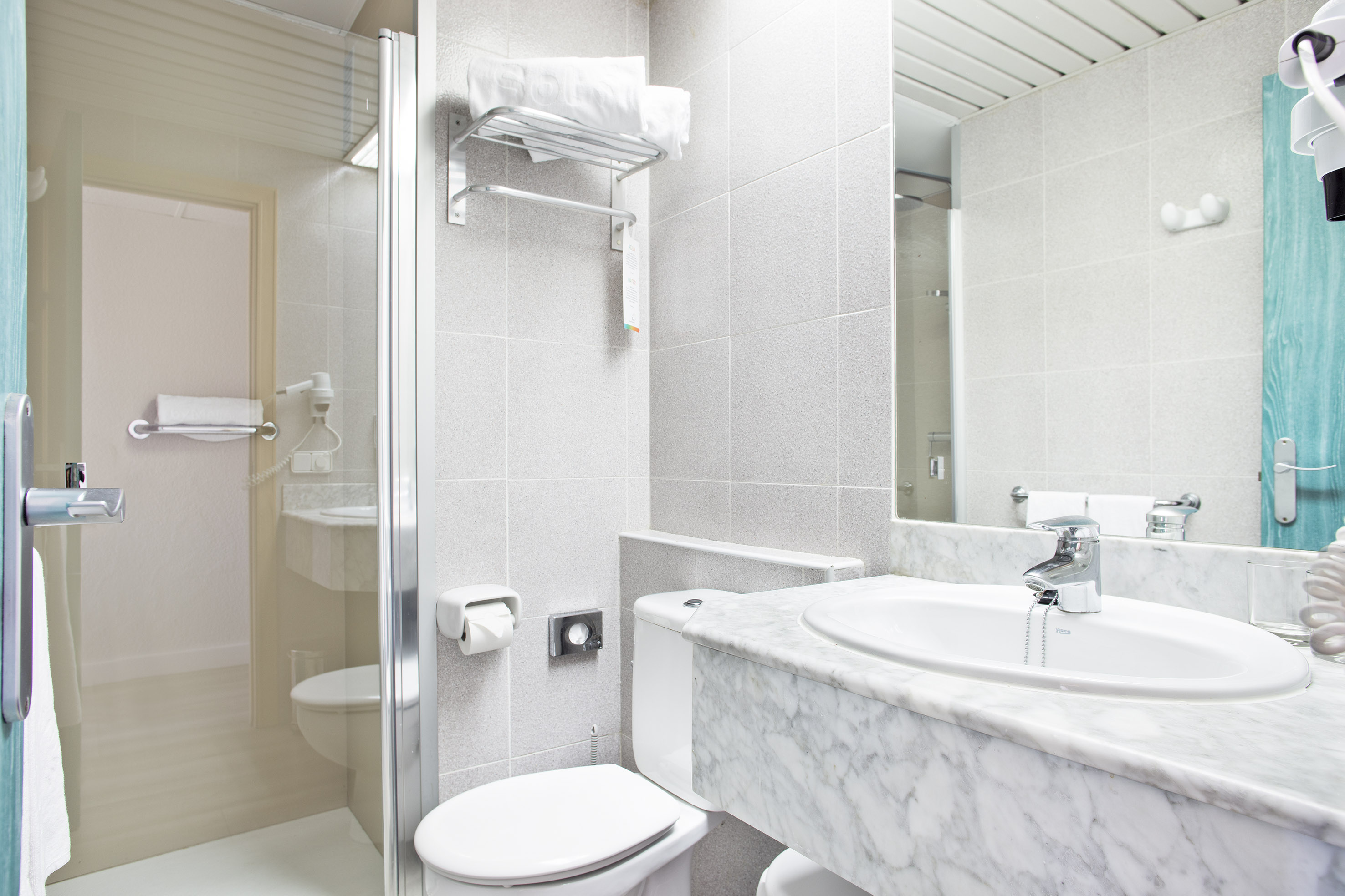 Hotel bathroom with glass shower, toilet, marble sink, and white tiled walls.