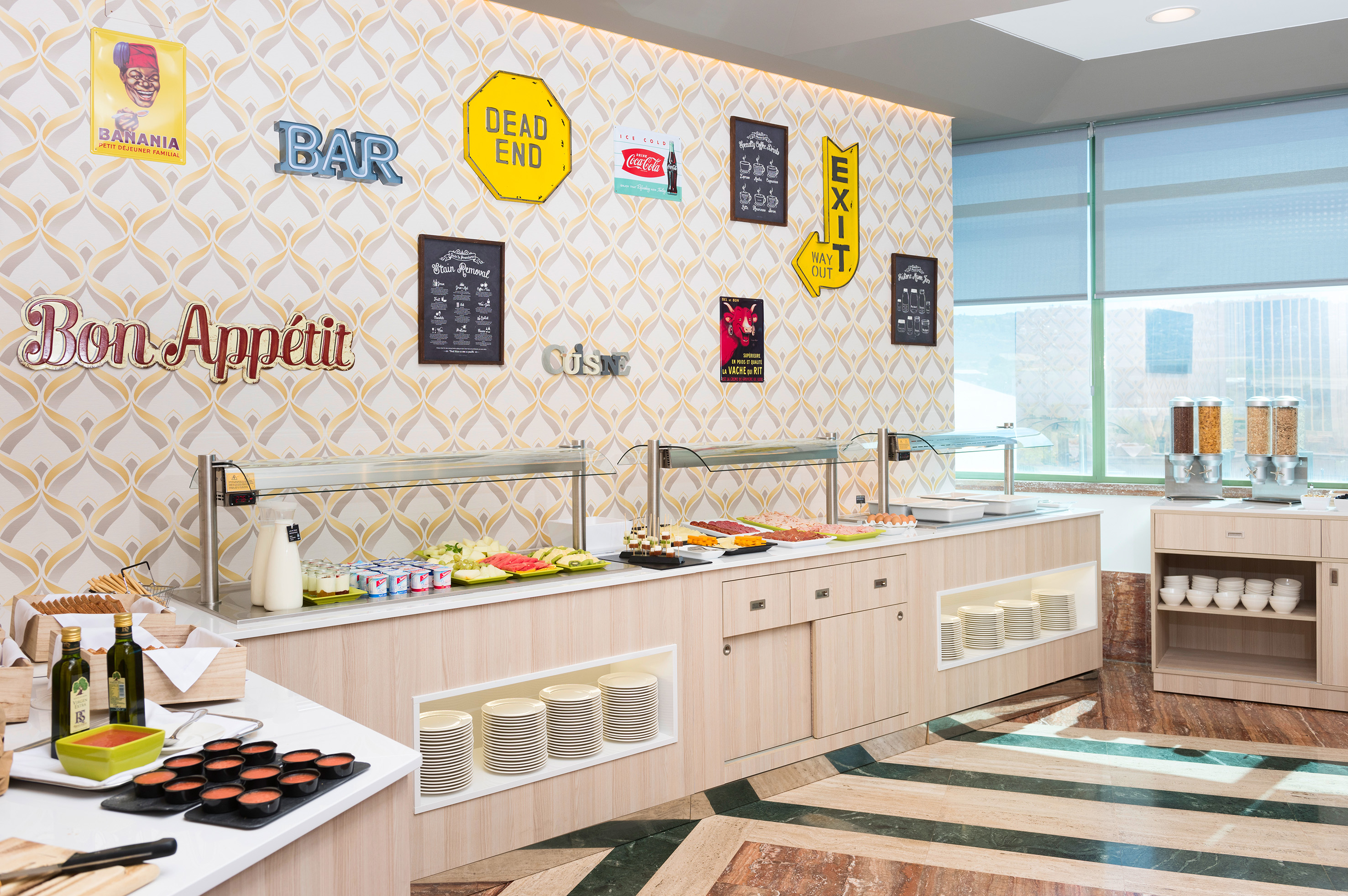 Modern hotel breakfast buffet with fresh food, cereals, and retro wall decor.