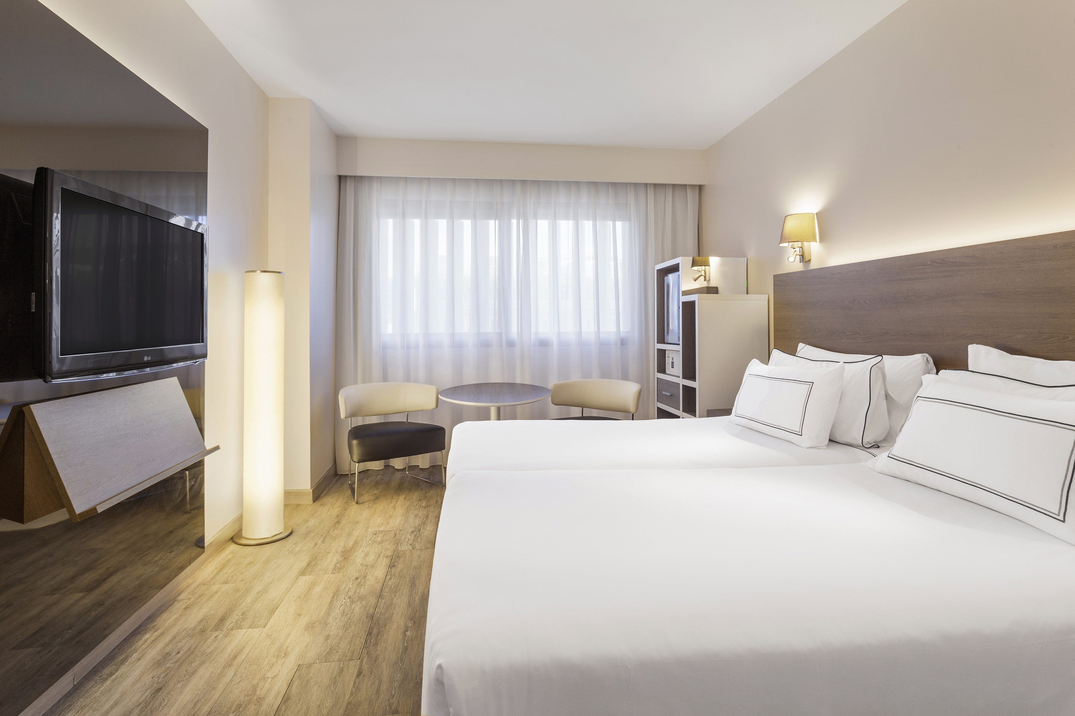 Contemporary hotel guest room with twin beds, TV, and window.