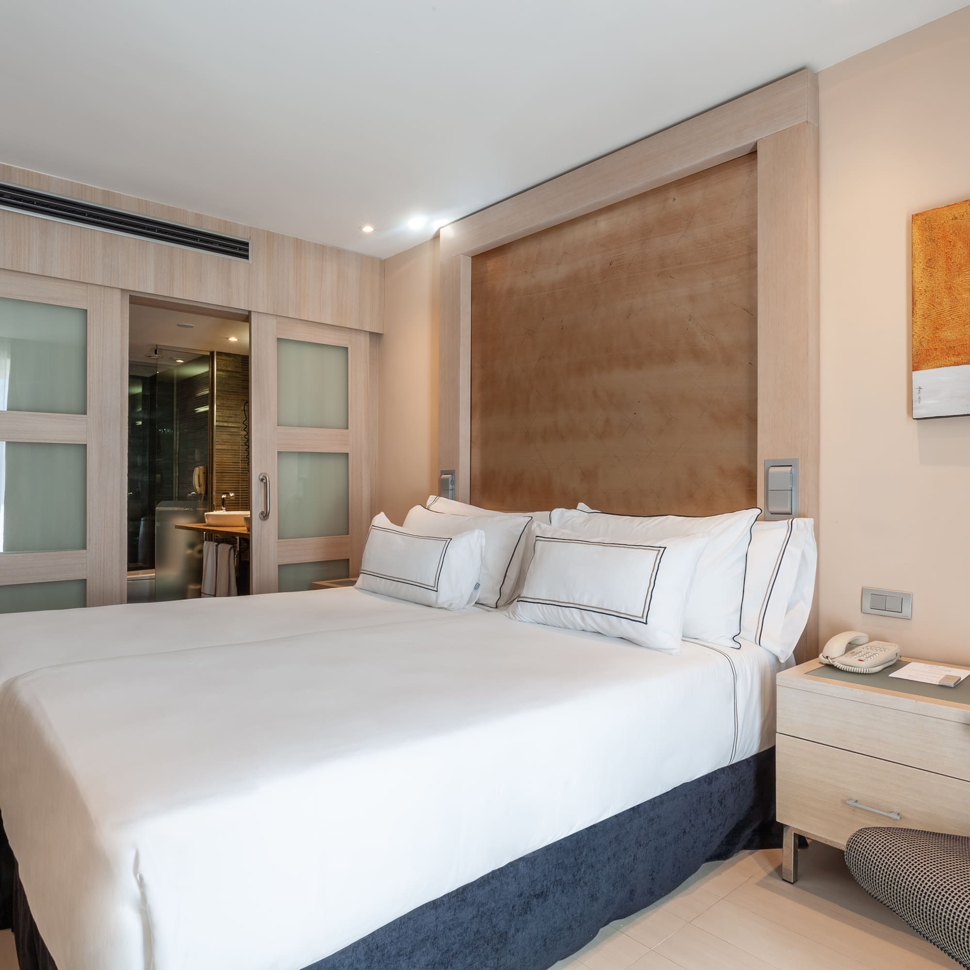 Modern hotel bedroom with white beds, wooden headboard, and ensuite bathroom.