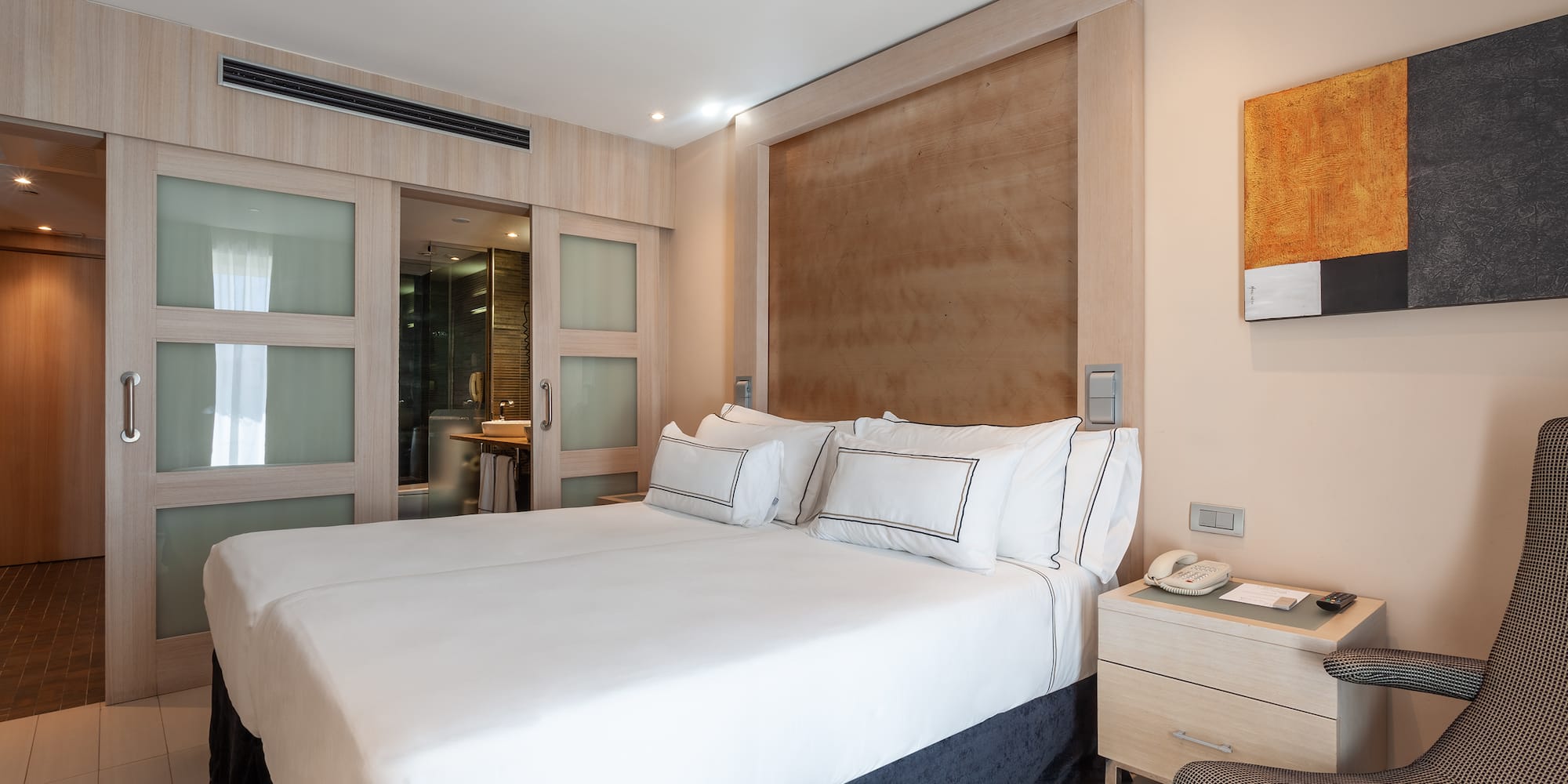 Modern hotel bedroom with white beds, wooden headboard, and ensuite bathroom.