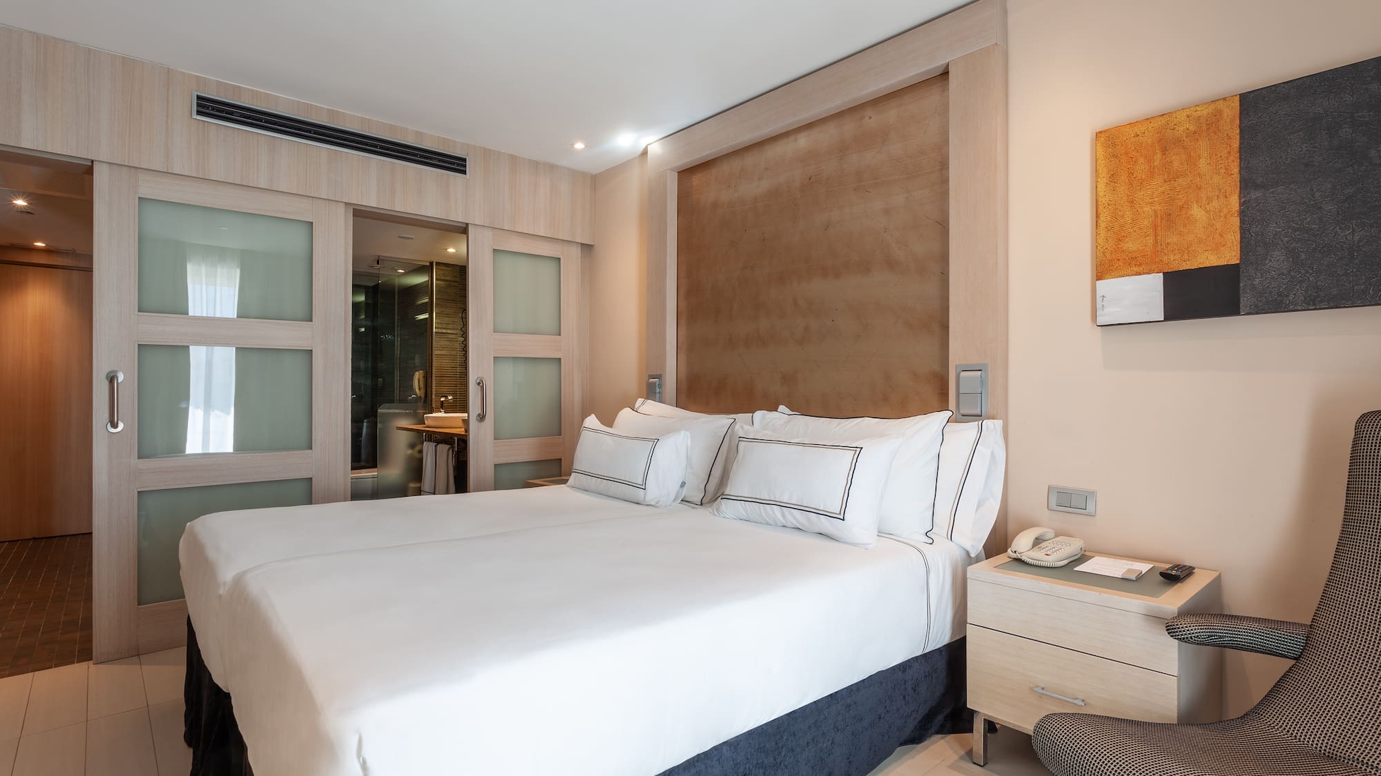 Modern hotel bedroom with white beds, wooden headboard, and ensuite bathroom.