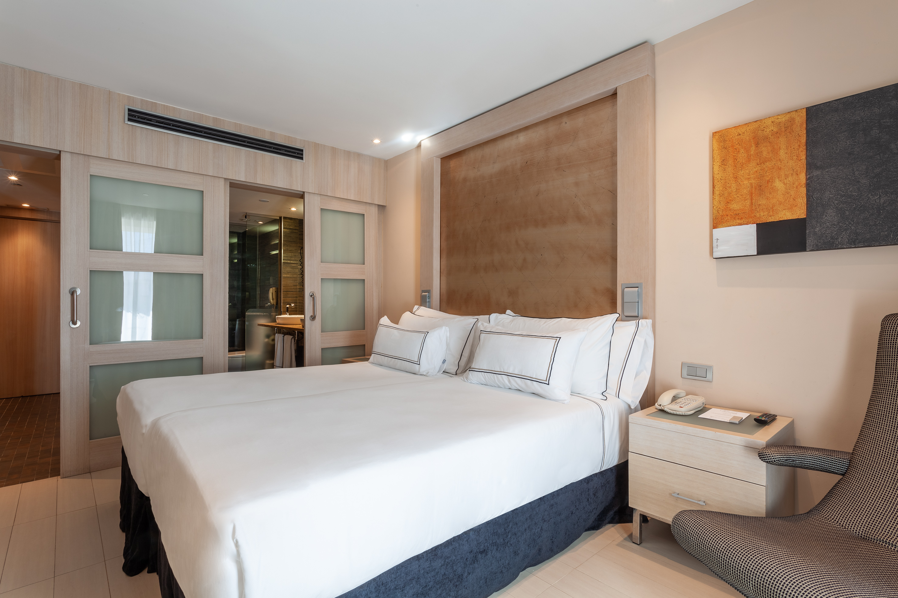 Modern hotel bedroom with white beds, wooden headboard, and ensuite bathroom.
