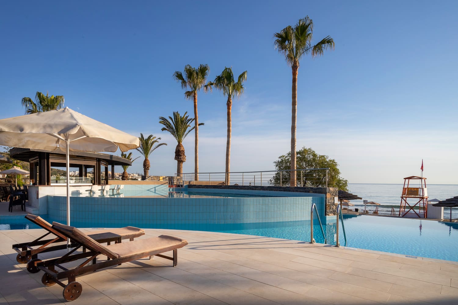 a pool with palm trees and a beach and a deck chair