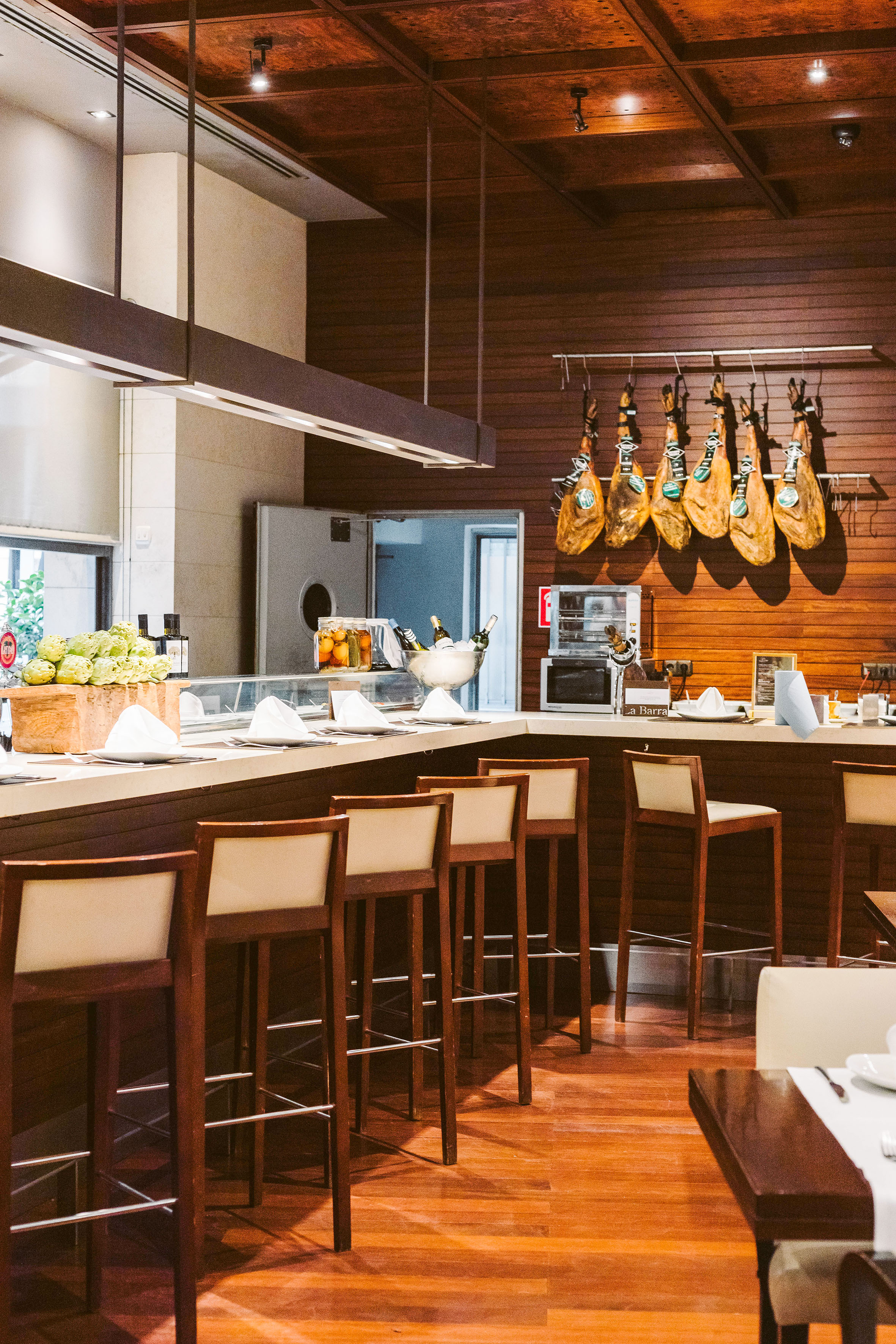 Spanish restaurant bar with hanging jamón legs and counter seating.