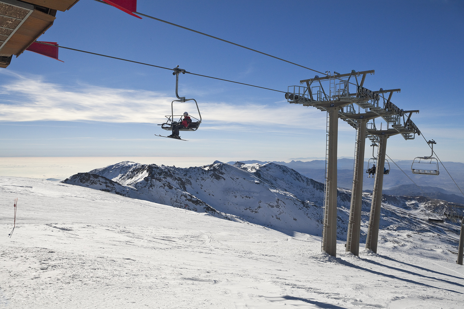 Skier riding a chairlift over snowy mountains under a clear blue sky.