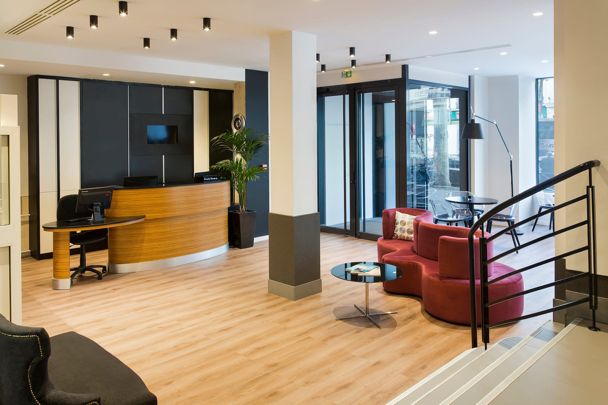 Modern hotel lobby with wood reception desk, red lounge seating, and glass entrance.
