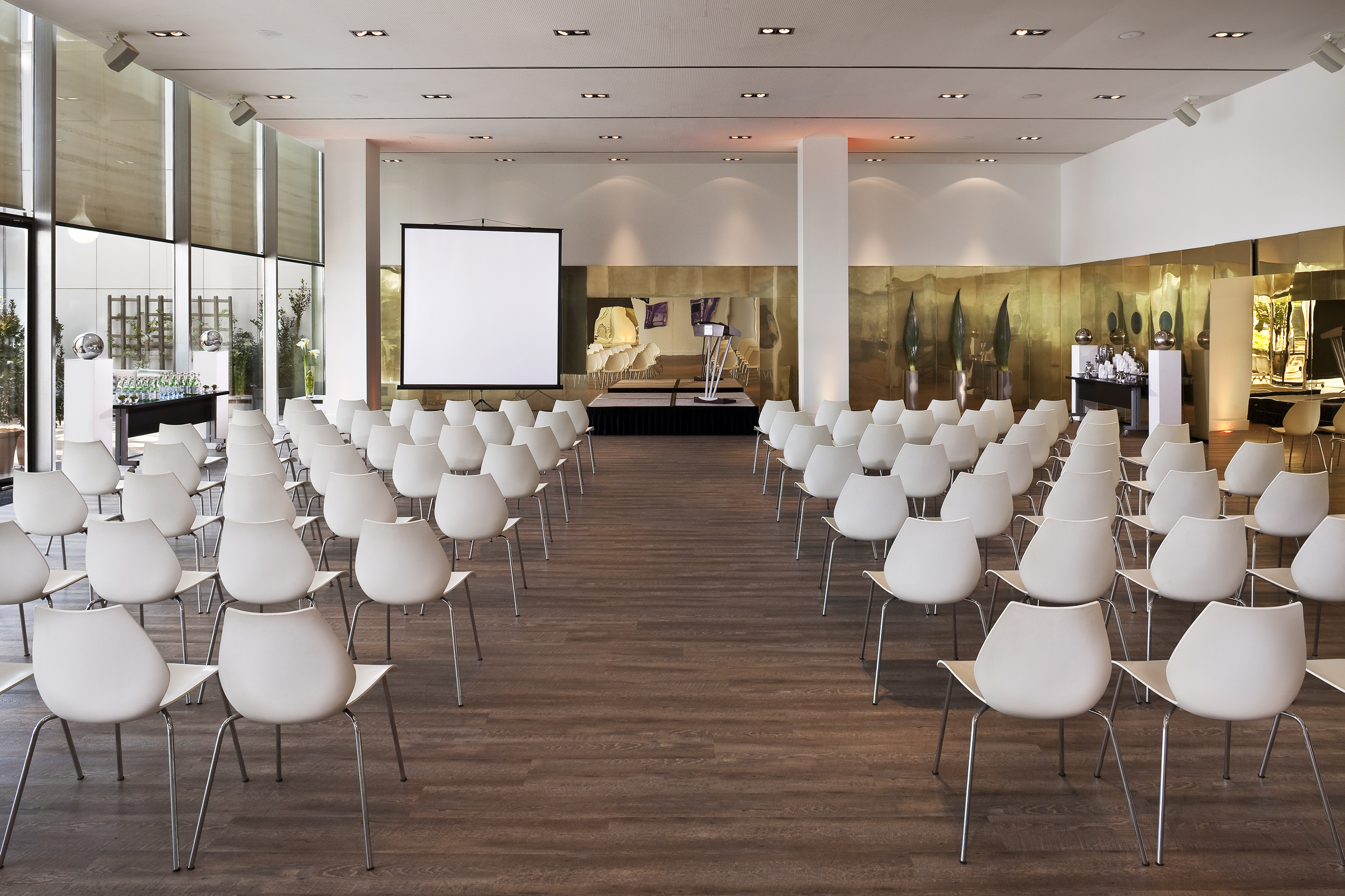 Modern conference room with white chairs, projector screen, and stage.