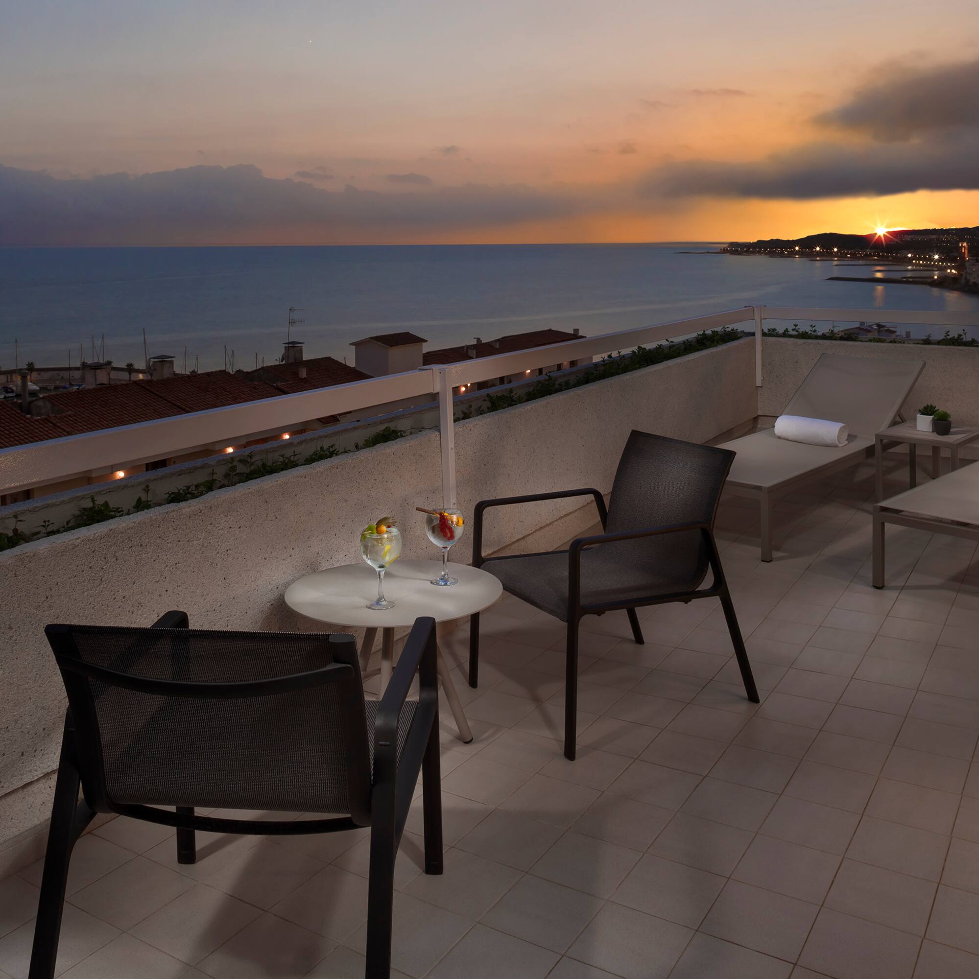 a patio with chairs and a table on a rooftop overlooking the ocean