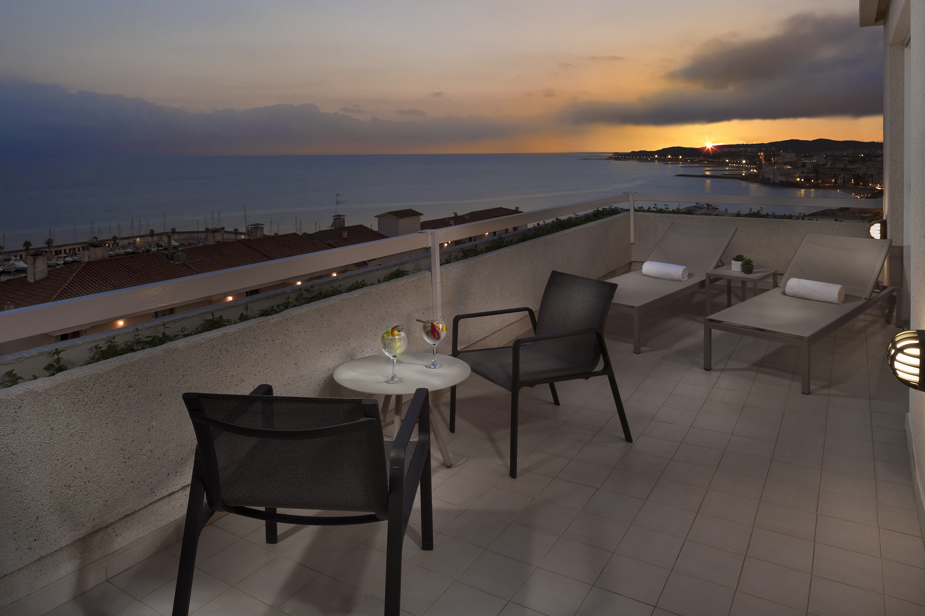 Ocean view balcony at sunset with cocktails, lounge chairs, and city lights.