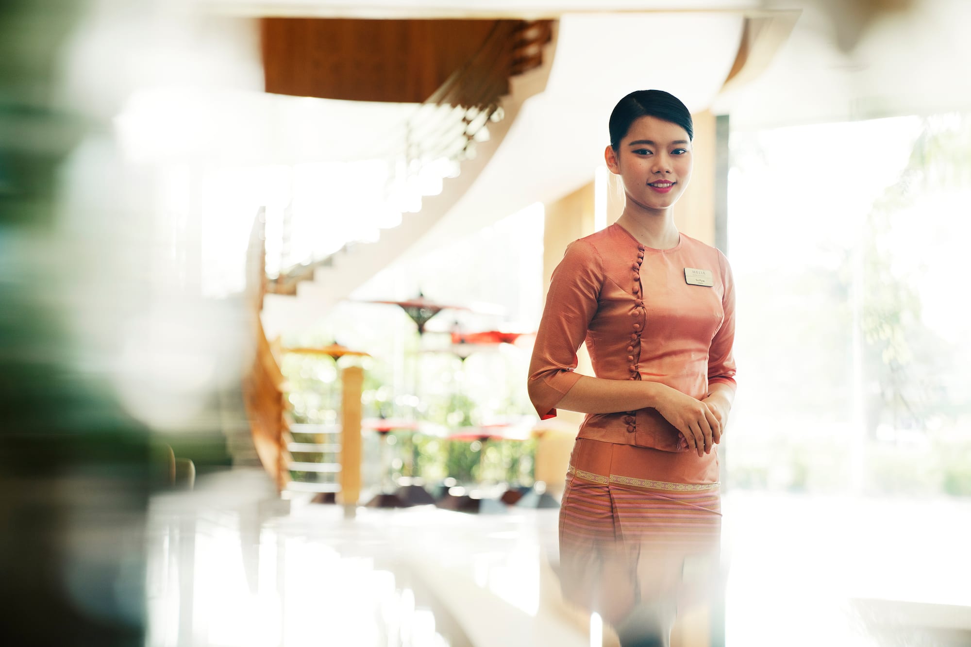 Smiling Melia hotel staff in traditional uniform, bright lobby background.