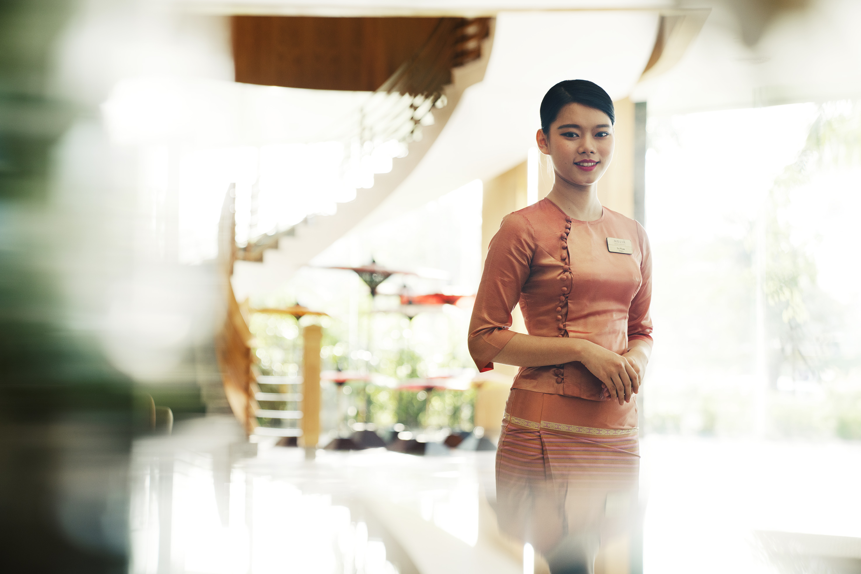 Smiling Melia hotel staff in traditional uniform, bright lobby background.